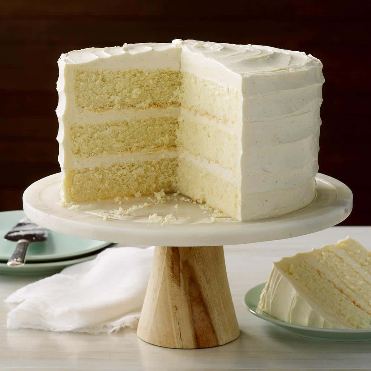 Buttercream 桌布 壁紙 — 一層層的雲呢拿蛋糕配白色糖霜，放在木架上，旁邊碟上有一片蛋糕。