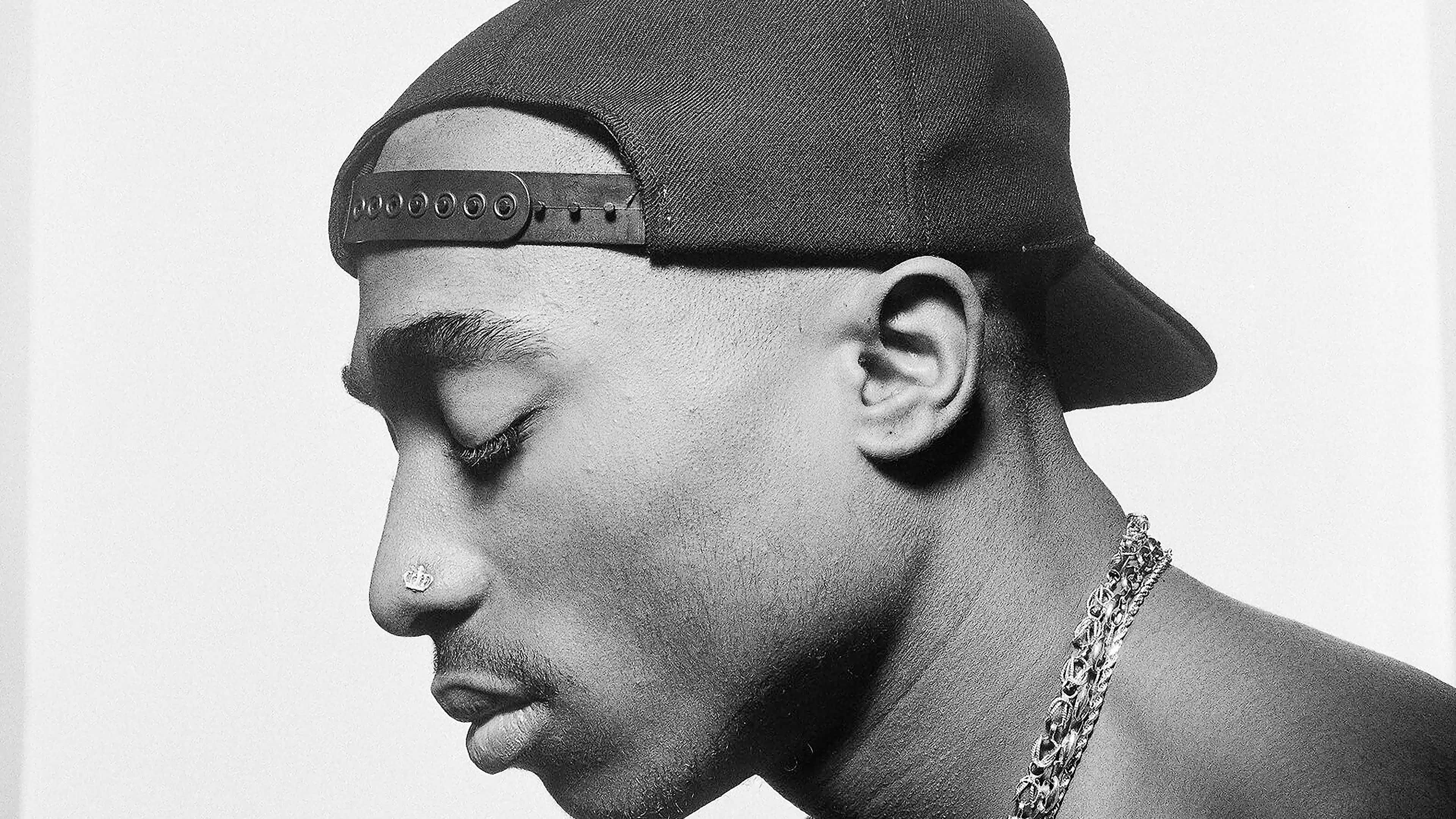 Tupac 桌布 壁紙 — 一幅Tupac Shakur的側面黑白肖像，戴著向後的帽子和鏈條項鍊，背景簡潔。