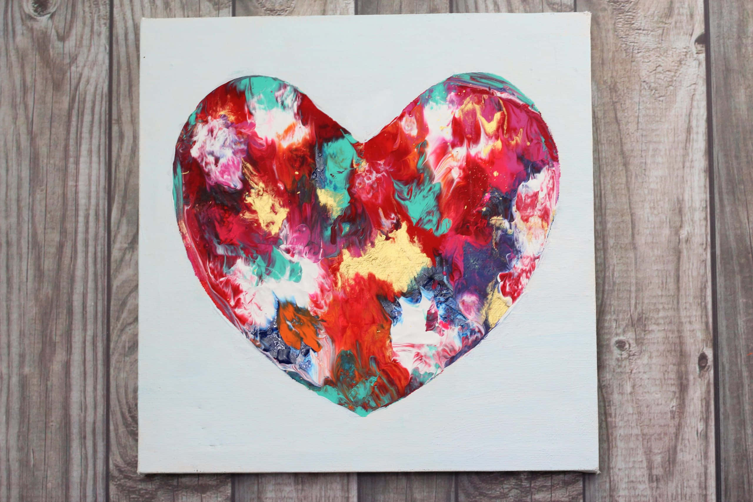 Heart Art 桌布 壁紙 — 一幅充滿活力的抽象心形畫作，帶有旋轉的紅色、藍綠色和金色，放置在質樸的木質表面上。