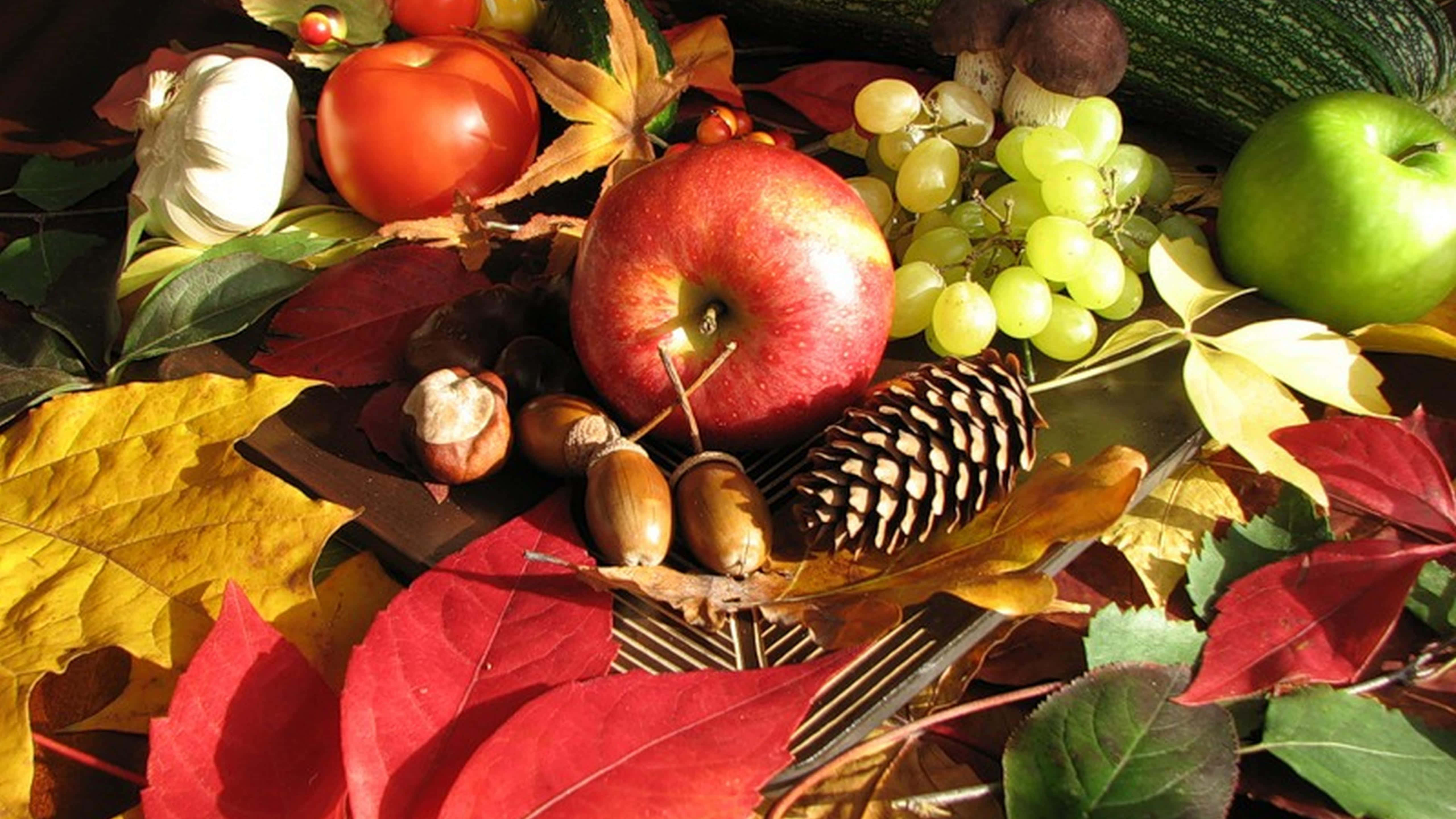 Fall Harvest 桌布 壁紙 — 一幅充滿活力的秋天靜物畫， featuring 紅蘋果、葡萄、松果和色彩繽紛的落葉，沐浴在溫暖的陽光下。