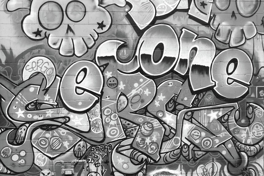 Black And White Graffiti 桌布 壁紙 — 一幅單色塗鴉覆蓋的磚牆，以混亂的城市藝術風格呈現粗體泡泡字母和帶有星星的卡通骷髏頭。