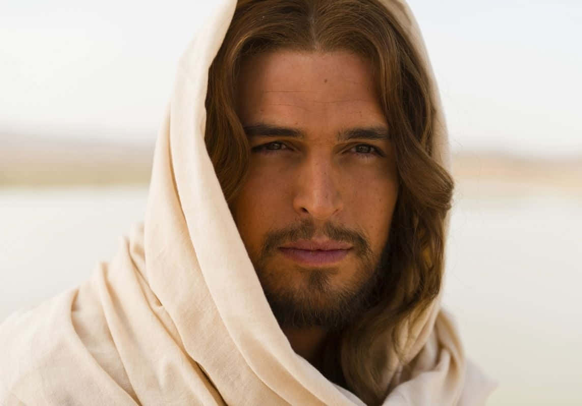 Son Of God 桌布 壁紙 — 一幅寧靜的肖像，一名長著棕色長髮和鬍鬚的男子，身披米色長袍，背景是朦朧的沙漠。