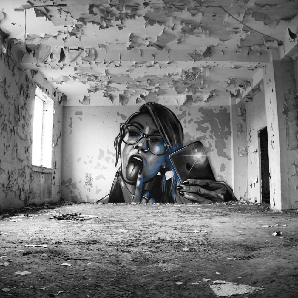 Black And White Graffiti 桌布 壁紙 — 一幅引人注目的黑白壁畫，描繪一位戴眼鏡的女性在破舊廢棄的房間裡舔手指，同時拿著手機。