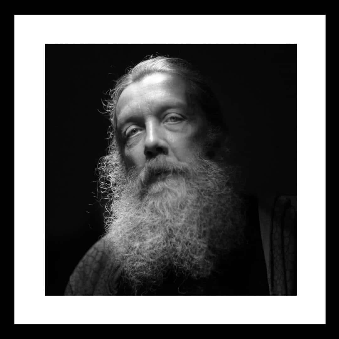 Alan Moore 桌布 壁紙 — 一幅戲劇性的黑白肖像，描繪一位鬍鬚男，眼神銳利，向上凝視，背景深暗。