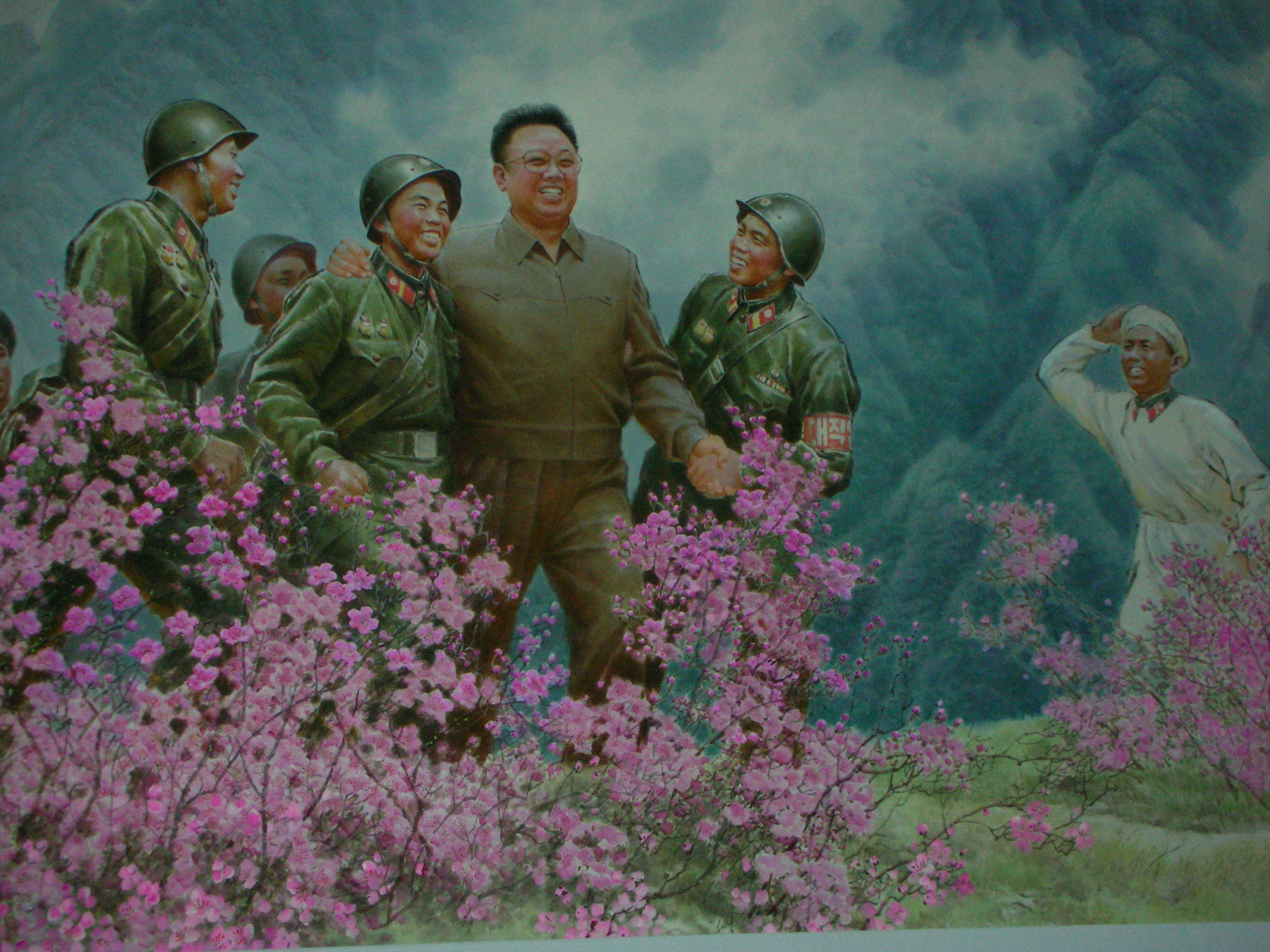 North Korea 桌布 壁紙 — 一幅繪畫場景顯示一個穿著平民服裝的中心人物在霧氣繚繞的山脈背景下，與身穿綠色制服的士兵們在鮮豔的粉紅色花叢中微笑。