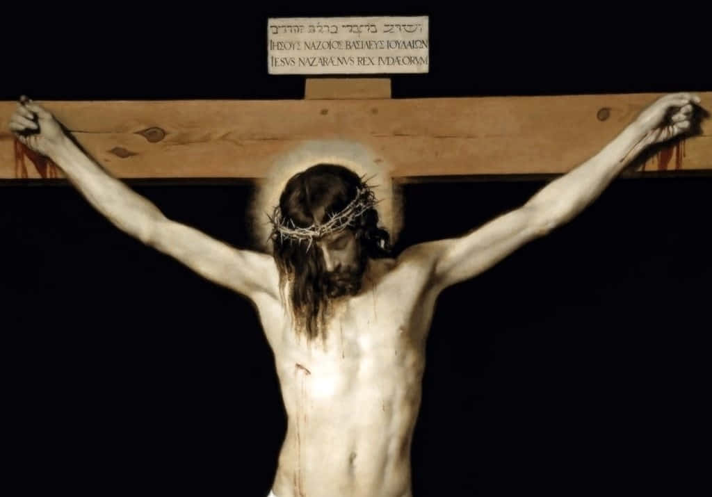 Jesus Crucifixion 桌布 壁紙 — 一幅莊嚴的描繪，耶穌基督被釘在木製十字架上，頭戴荊棘冠冕，帶有光環，背景為深色。