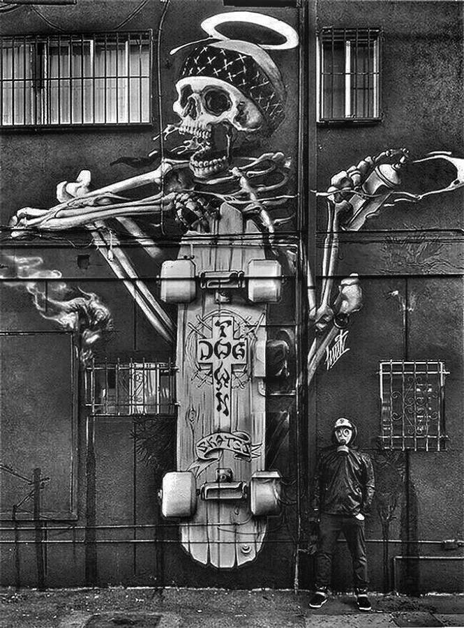Black And White Graffiti 桌布 壁紙 — 一幅黑白壁畫，描繪一個帶光環和頭巾的骷髏滑板手，主宰著粗糙的城市牆壁，下方站著一個戴頭盔的人。