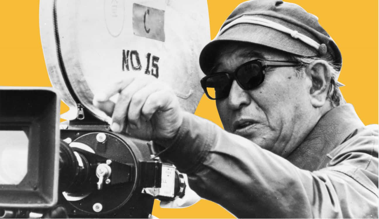 Akira Kurosawa 桌布 壁紙 — 一幅黑白肖像，一位電影製作人在大膽的黃色背景前操作一部復古電影攝影機。