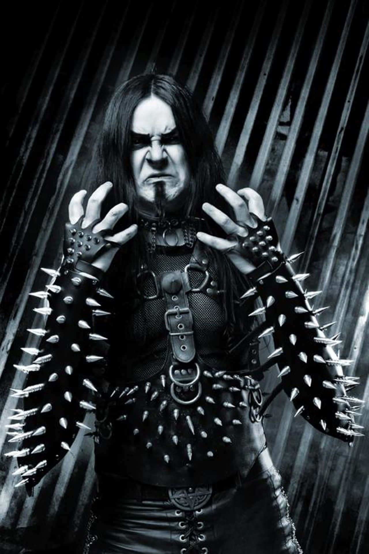 Black Metal Music 桌布 壁紙 — 一幅黑白肖像，描繪一位帶有威脅性的哥德音樂家，戴著尖刺手套和皮革裝備，背景為波紋金屬板。