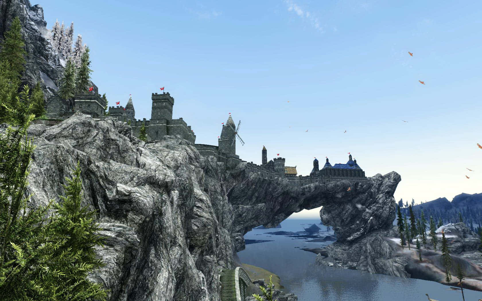 Skyrim Solitude 桌布 壁紙 — 一座中世紀城堡坐落在一個巨大的天然石拱門頂部，橫跨寧靜的河谷，上方是清澈的藍天。