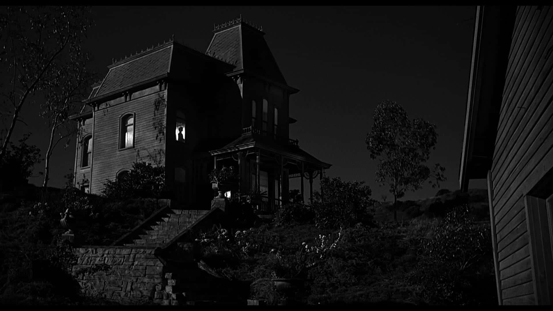 Black And White Film 桌布 壁紙 — 一座令人毛骨悚然的黑白維多利亞式房屋在夜間孤立地矗立在山丘上，一扇窗戶發出不祥的光芒。