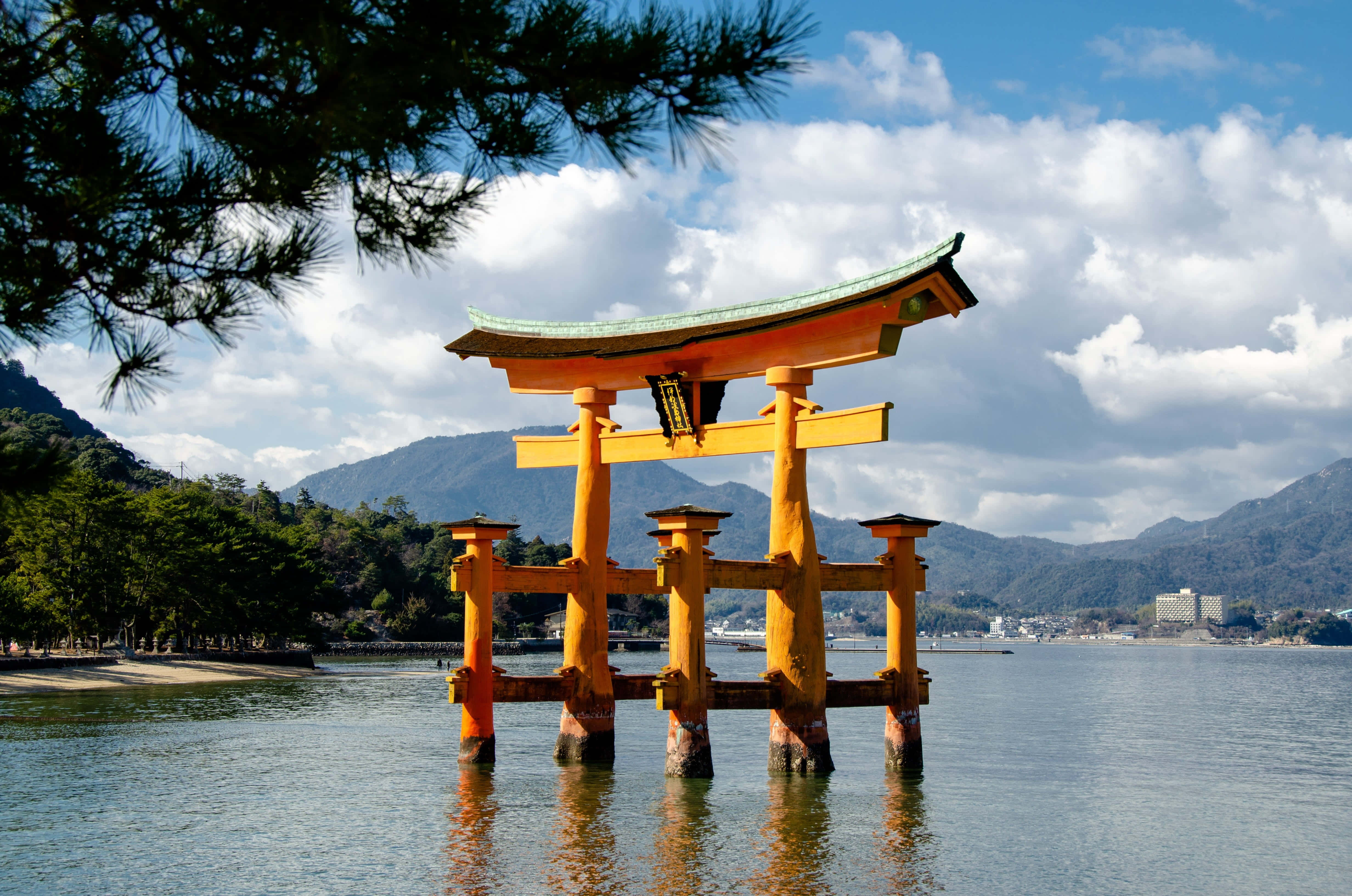 Shinto 桌布 壁紙 — 一座充滿活力的橙色鳥居在平靜的水面上巍然聳立，背景是晴朗的藍天和蓬鬆的白雲。