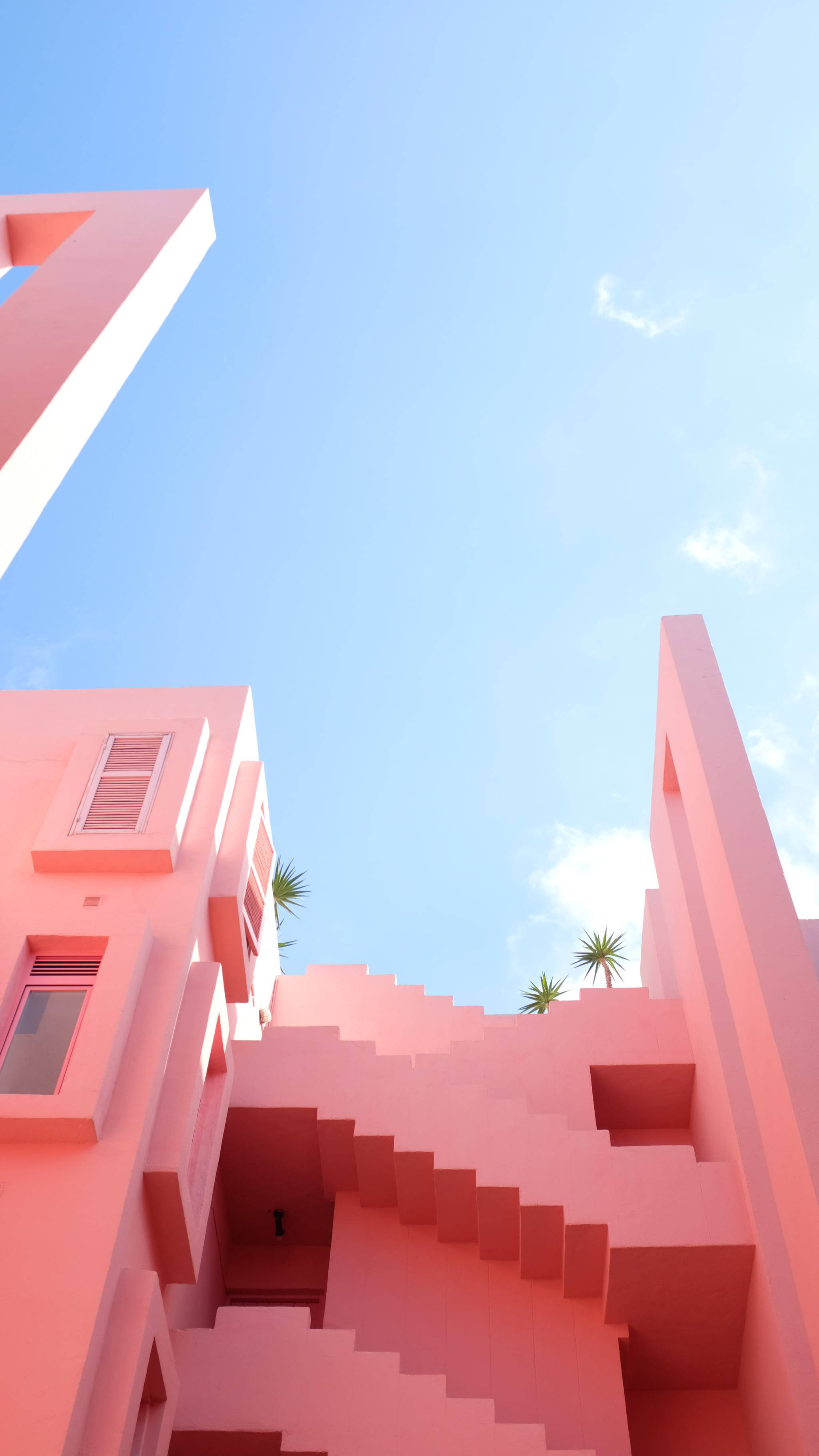 Building 桌布 壁紙 — 一座充滿活力的粉紅色幾何建築，擁有醒目的樓梯和窗戶，位於清澈藍天和稀疏白雲之下。