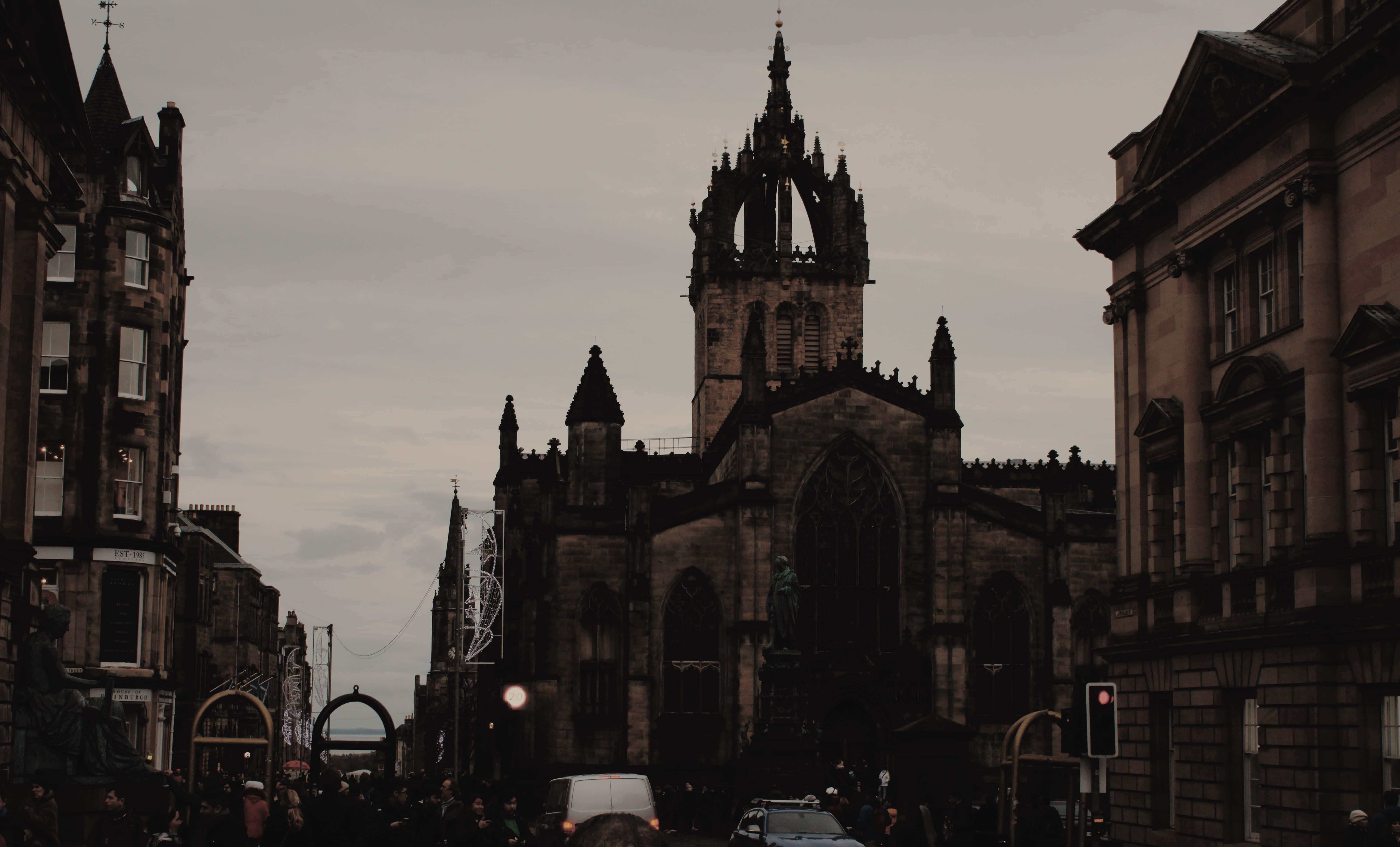 Dark Academia Aesthetic 桌布 壁紙 — 一座哥德式大教堂聳立在狹窄的城市街道上，陰沉多雲的天空下，兩旁是歷史建築。