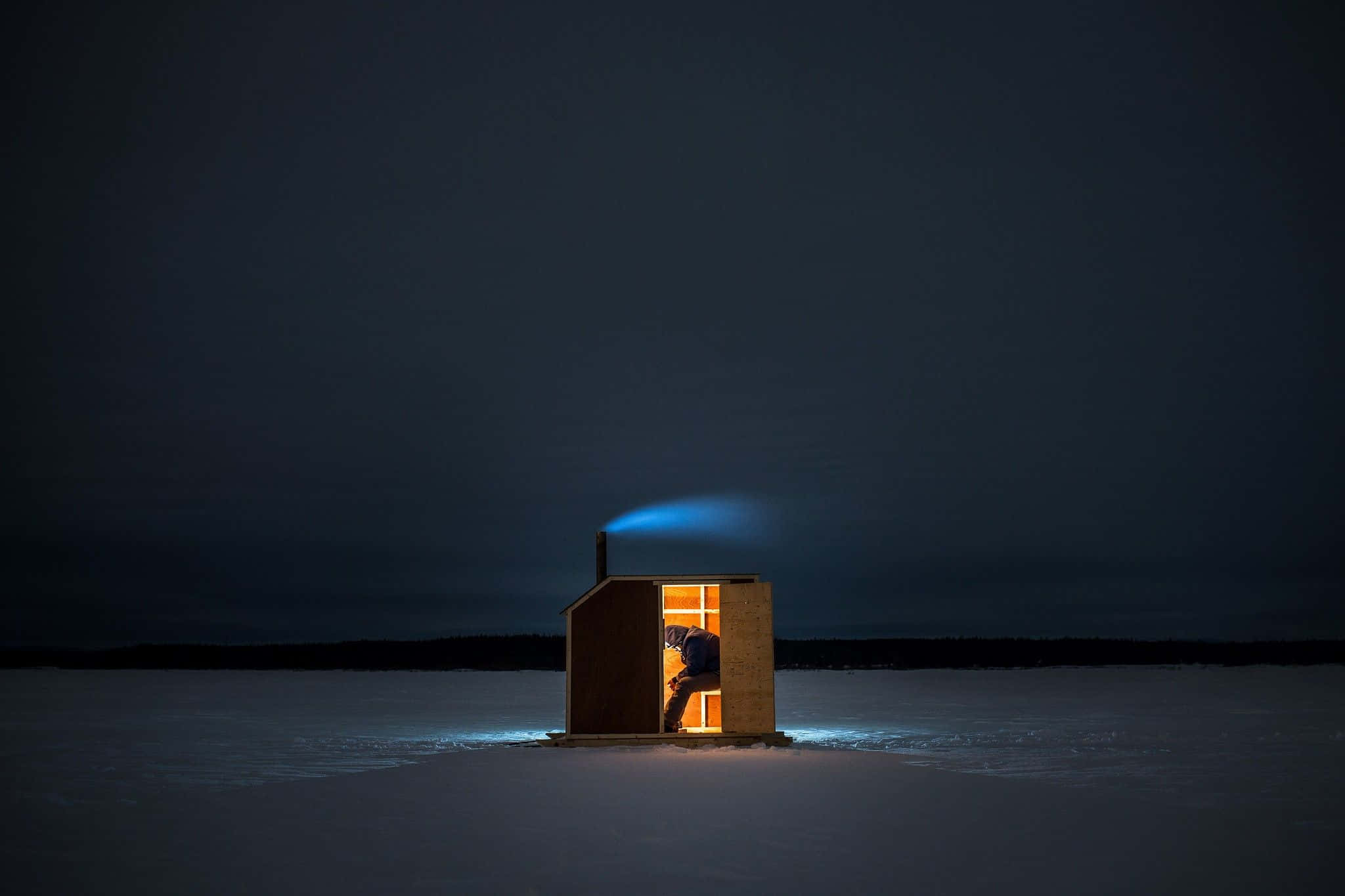 Ice Fishing 桌布 壁紙 — 一座孤獨的木造桑拿在結冰的湖面上於夜晚溫暖地發光，煙囪中升起藍色蒸汽柱。