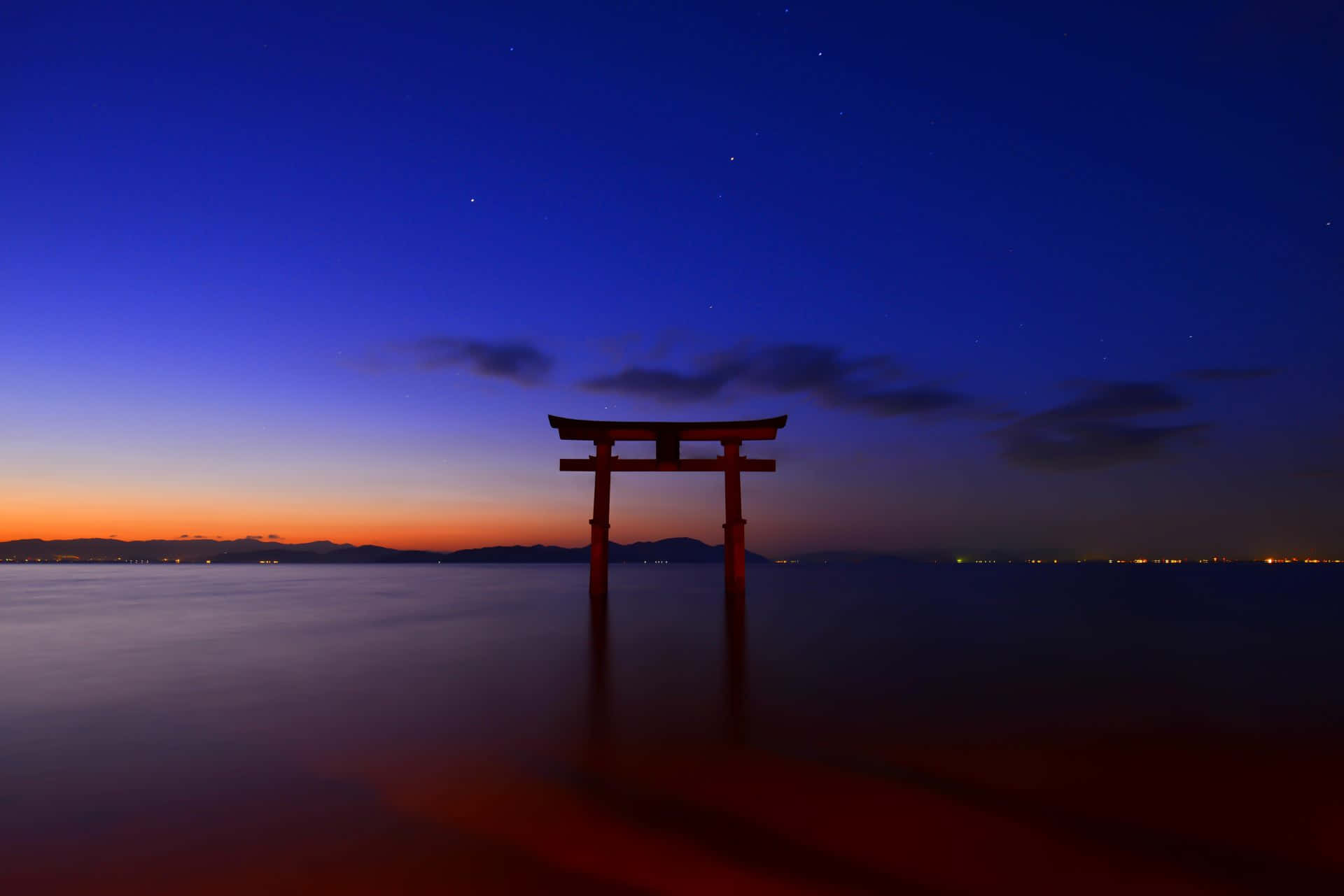 Shinto 桌布 壁紙 — 一座孤獨的紅色鳥居矗立在平靜的水面上，天空暮色中帶有橙色和深藍色星星的條紋。