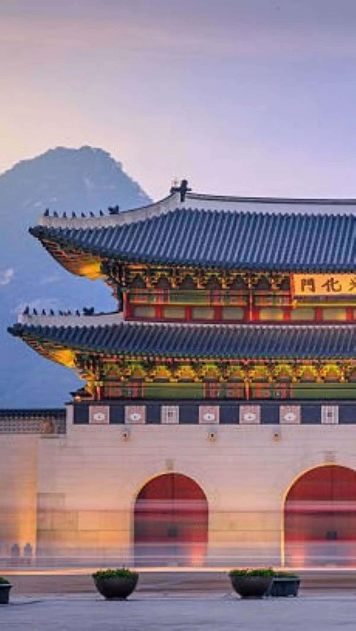 South Korea 桌布 壁紙 — 一座宏偉的傳統韓國大門在黃昏時亮起，背景是山脈，下方有模糊的動態。