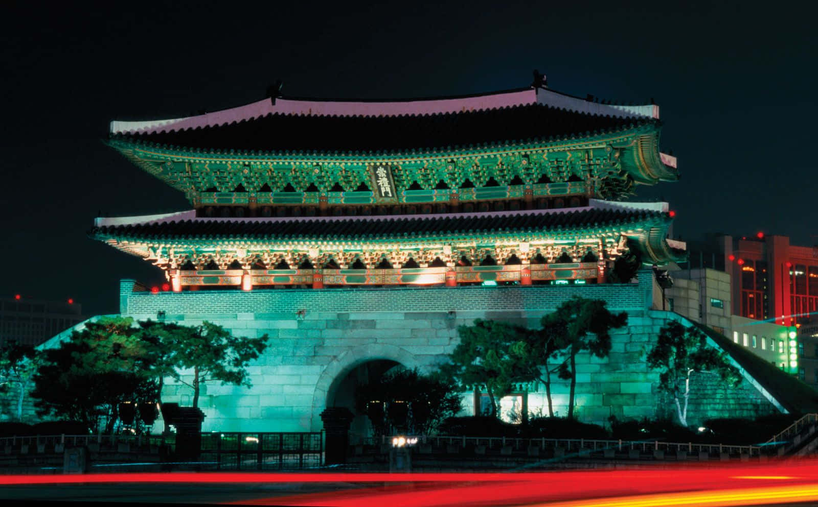 South Korea 桌布 壁紙 — 一座宏偉的傳統韓國門樓在夜晚以綠色和紅色燈光照明，下方有汽車燈光形成的條紋。