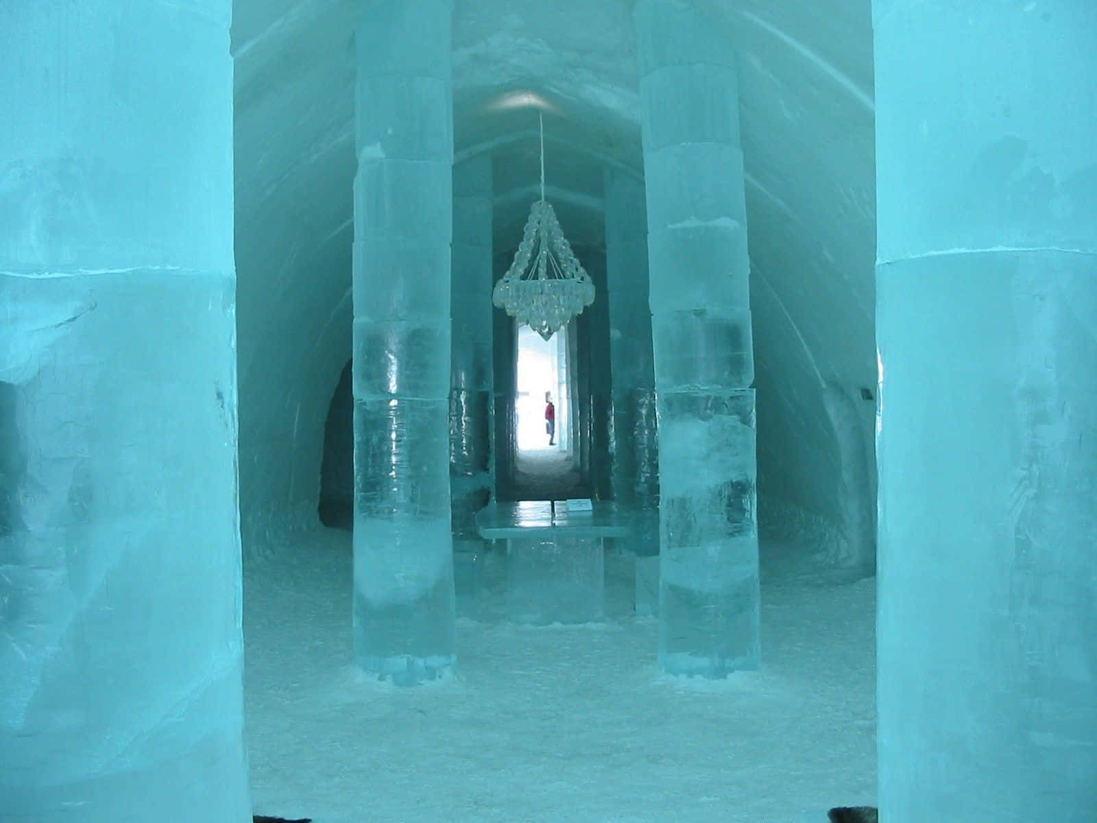 Ice Hotel 桌布 壁紙 — 一座宏偉的冰教堂，高聳的柱子和吊燈懸掛在冰冷的藍色光芒中。
