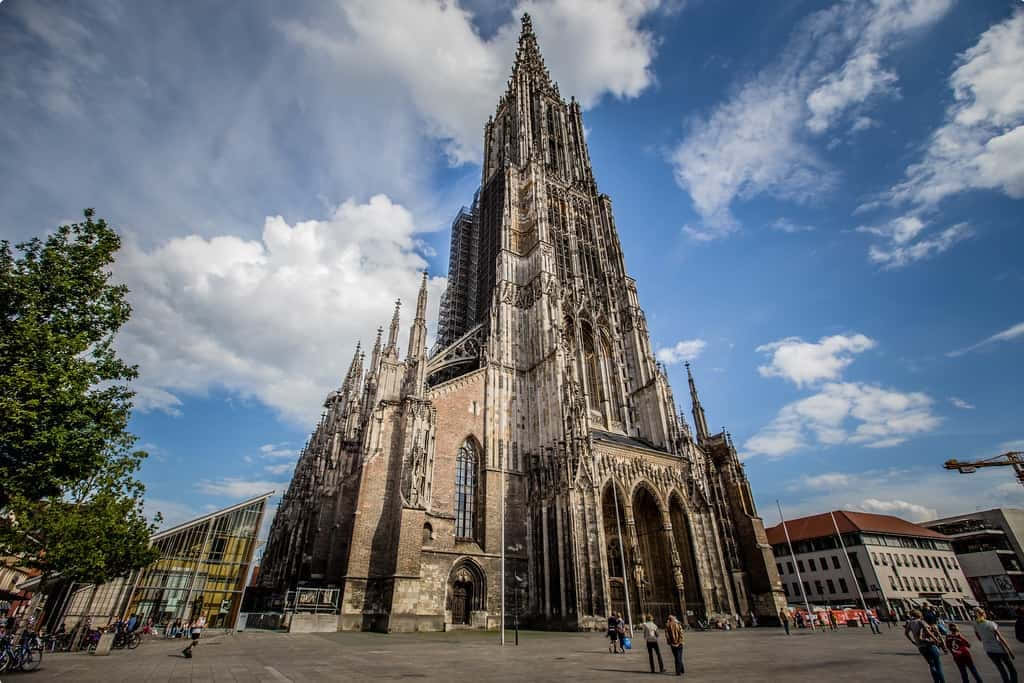 Gothic Architecture 桌布 壁紙 — 一座宏偉的哥德式大教堂，擁有複雜的尖塔和飛扶壁，在晴朗的藍天和蓬鬆的白雲映襯下巍然聳立。