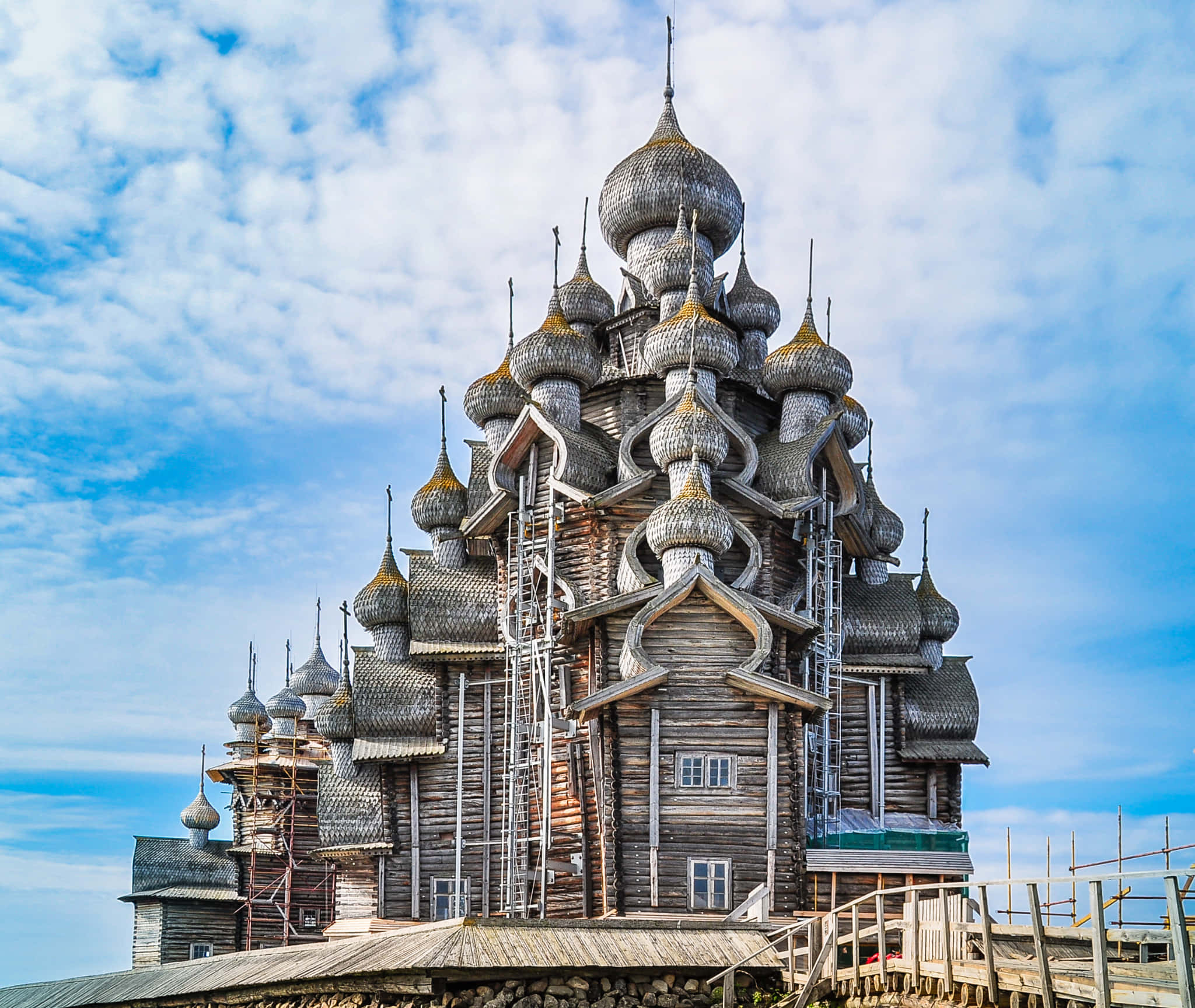 Beautiful Architecture 桌布 壁紙 — 一座宏偉的木製教堂，有多個洋蔥形圓頂，在明亮的藍天和散落的雲朵下。