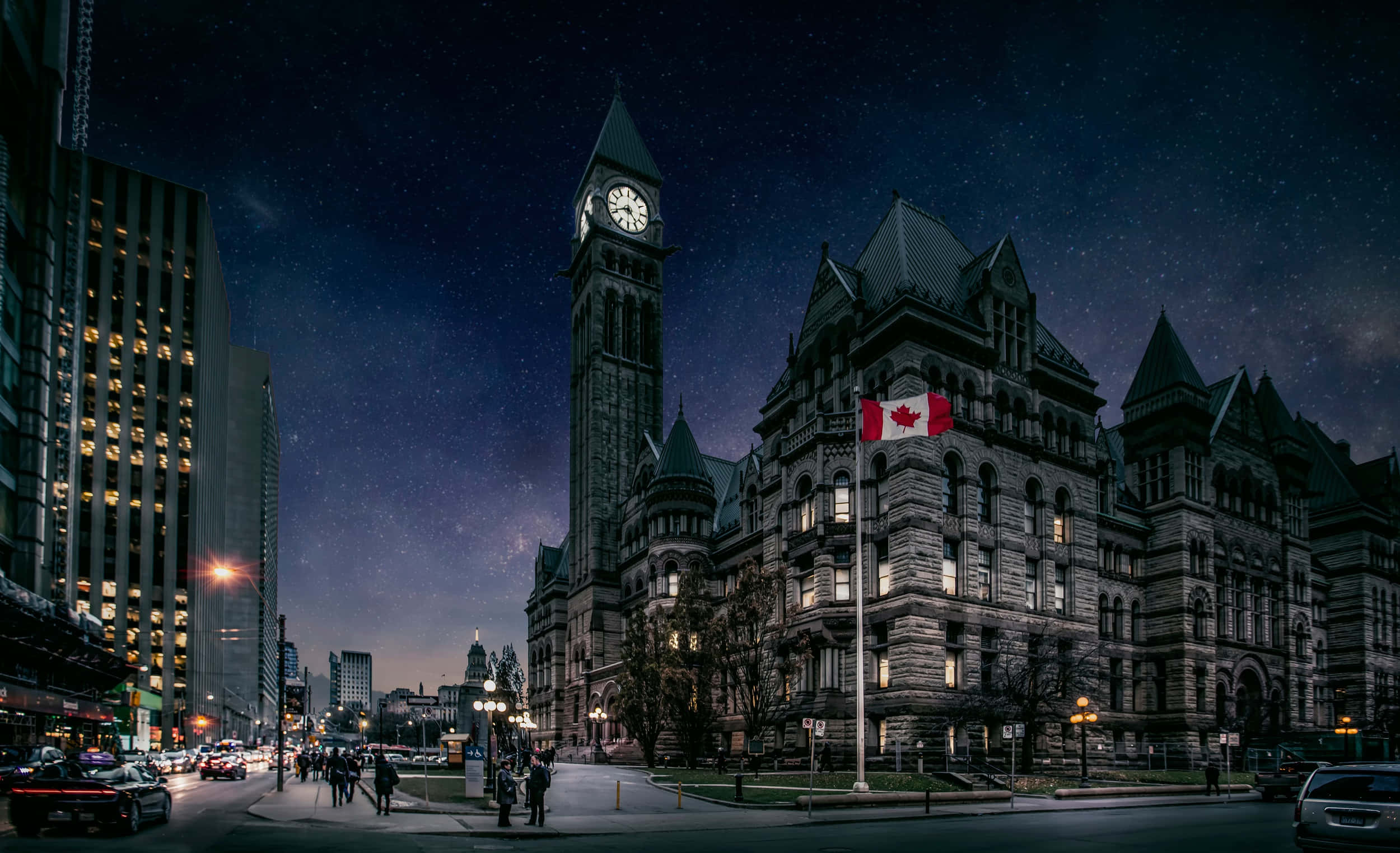 Canada 桌布 壁紙 — 一座宏偉的歷史石建築，帶有鐘樓和加拿大國旗，矗立在星空下，旁邊是現代摩天大樓和城市街道。