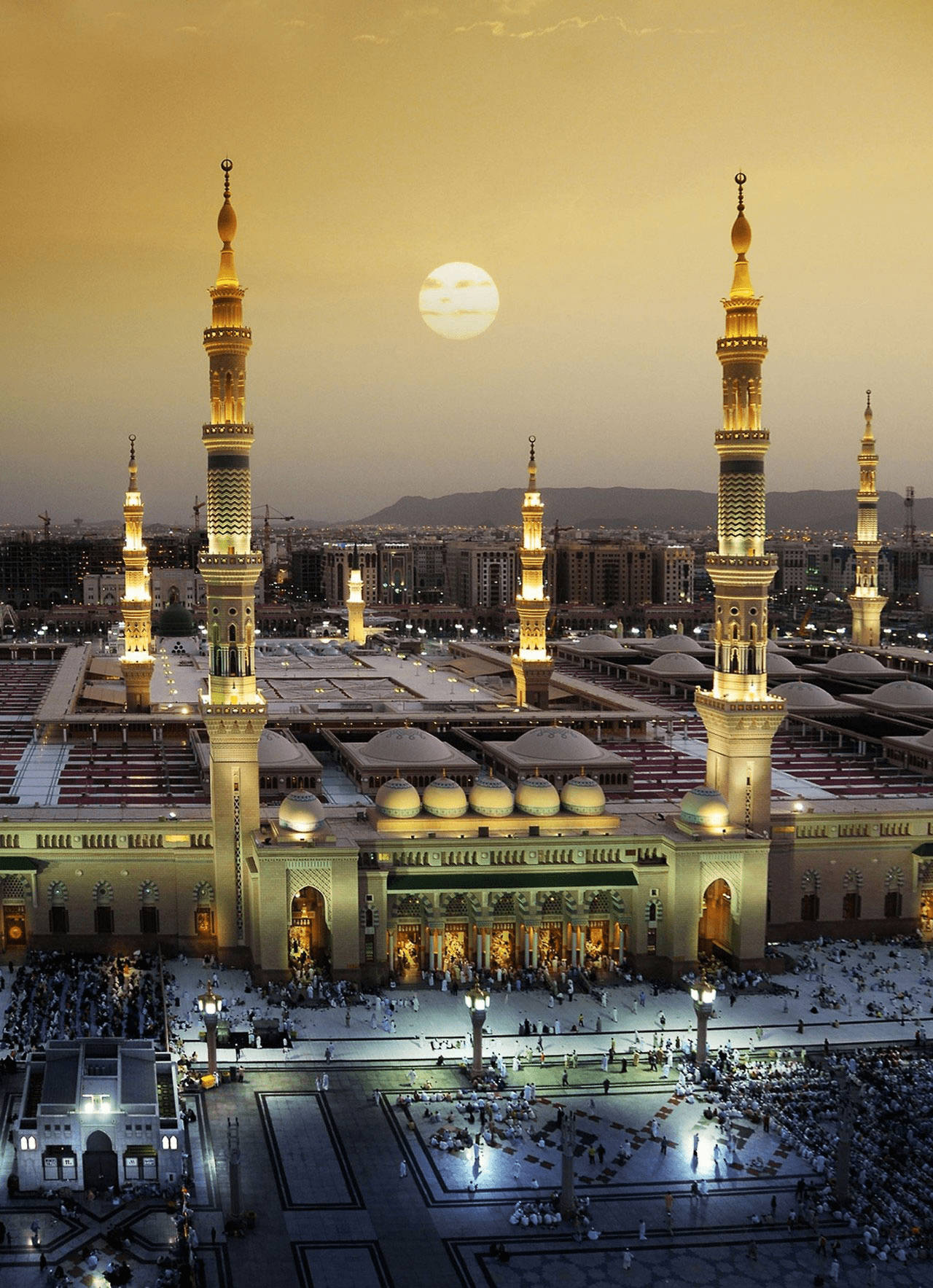 Madina Sharif 桌布 壁紙 — 一座宏偉的清真寺，在金色日落天空和滿月下，有燈光璀璨的宣禮塔和圓頂。