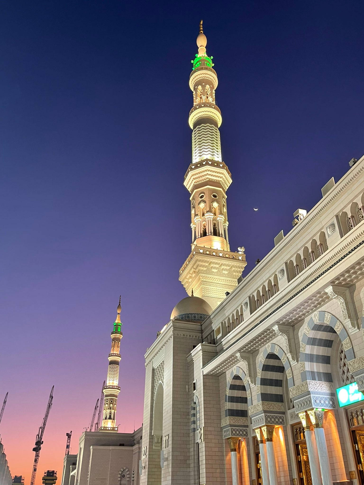 Madina Sharif 桌布 壁紙 — 一座宏偉的清真寺，尖塔燈火通明，在暮色天空中升起，可見一彎新月。