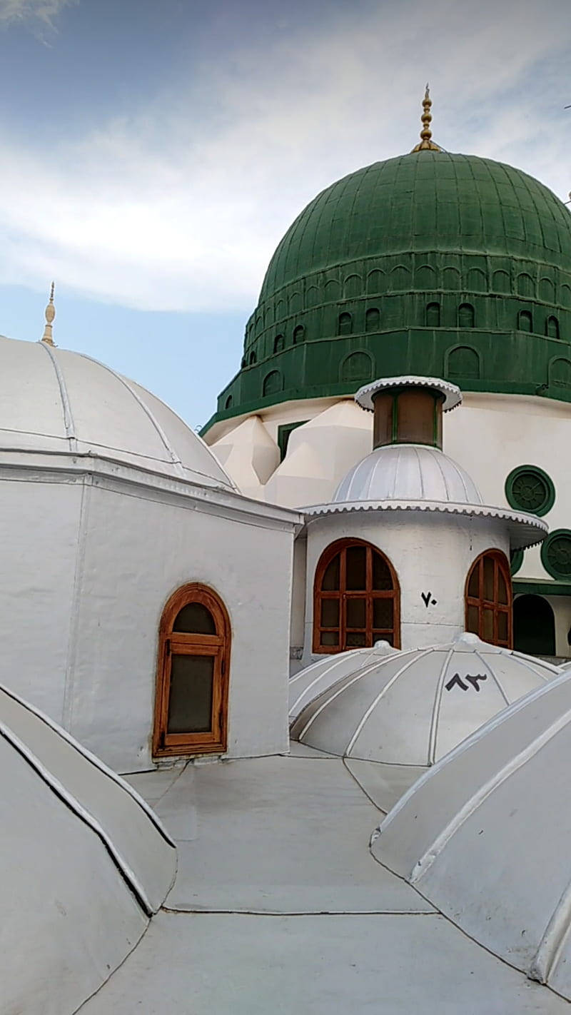 Madina Sharif 桌布 壁紙 — 一座宏偉的清真寺，擁有大型綠色圓頂和白色圓頂，天空部分多雲。