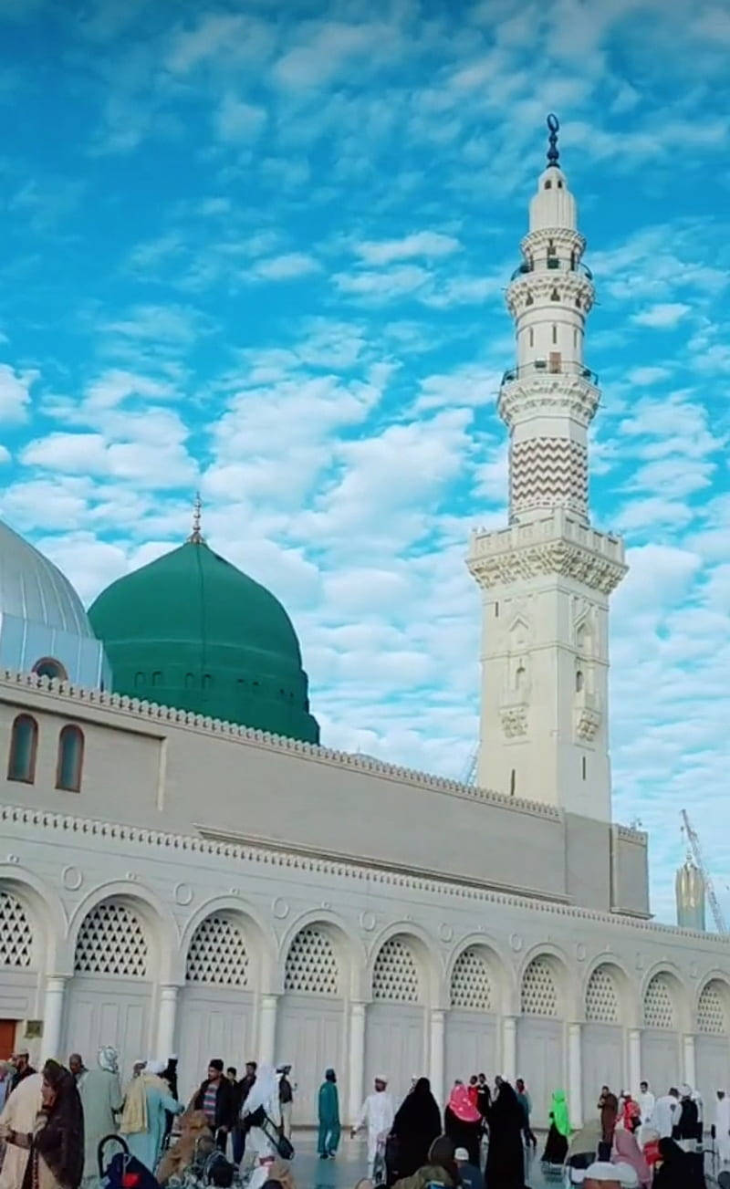 Madina Sharif 桌布 壁紙 — 一座宏偉的白色清真寺，擁有綠色圓頂和高聳的宣禮塔，矗立在點綴著蓬鬆雲朵的鮮豔藍天下。