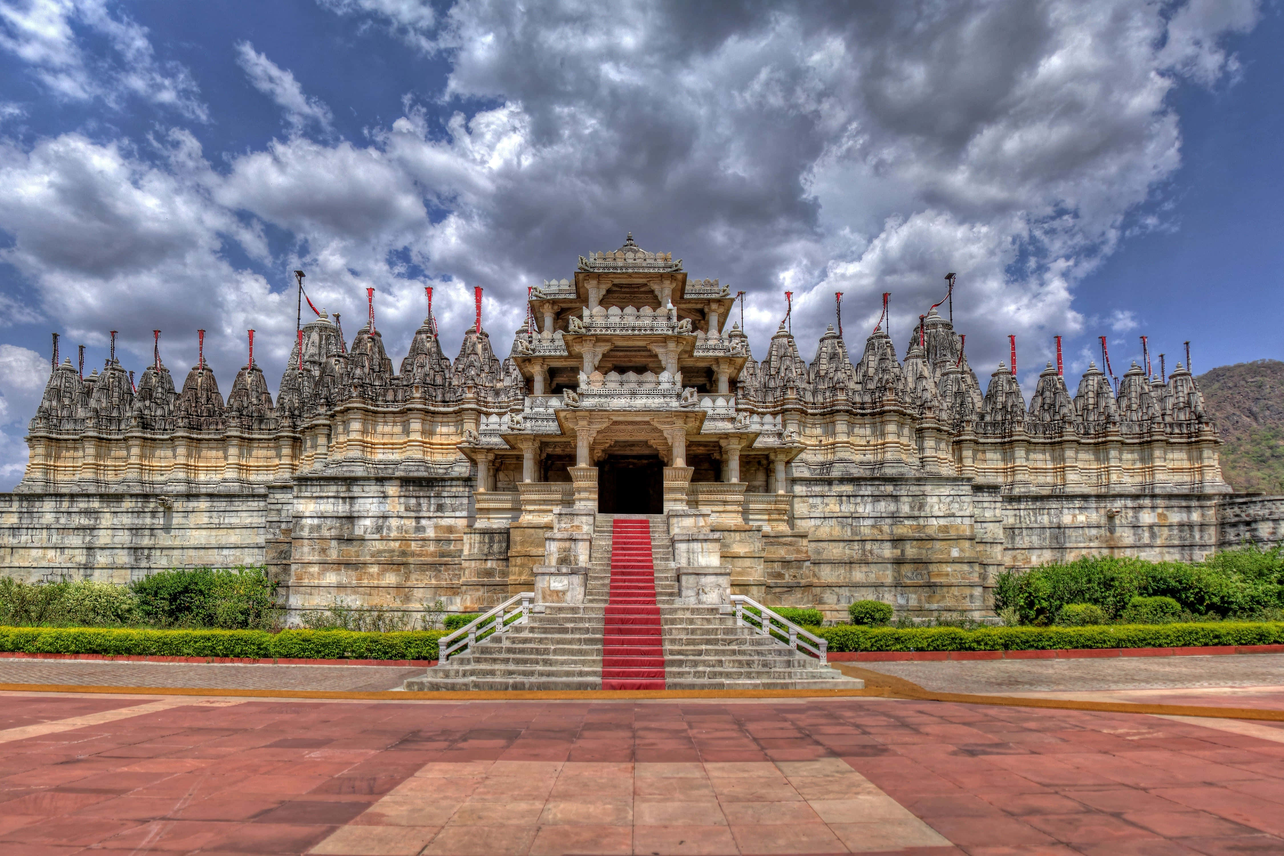 Rajasthan 桌布 壁紙 — 一座宏偉的石廟，雕刻精細，在戲劇性的多雲天空下鋪有紅色地毯的樓梯。