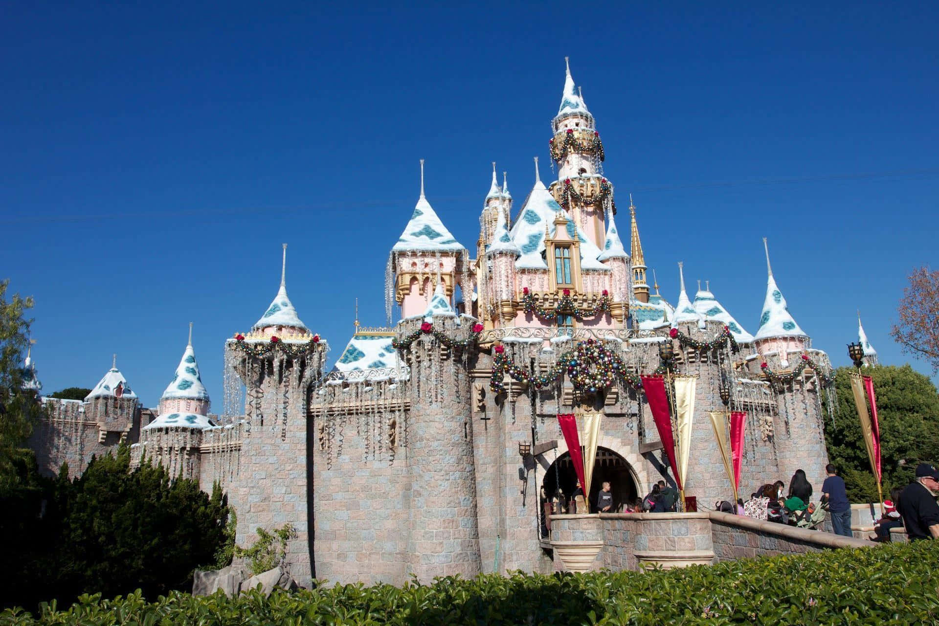Disneyland 桌布 壁紙 — 一座宏偉的童話城堡，擁有積雪覆蓋的塔樓和節日花環，矗立在清澈的藍天下。
