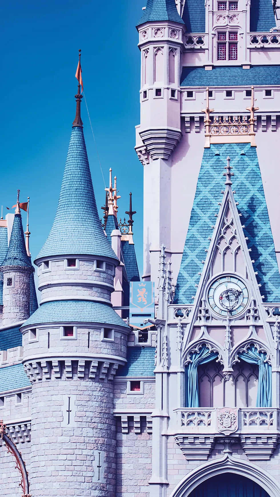 Disney Castle 桌布 壁紙 — 一座宏偉的童話城堡，擁有藍色瓷磚屋頂和華麗的塔樓，在清澈的藍天下巍然聳立。
