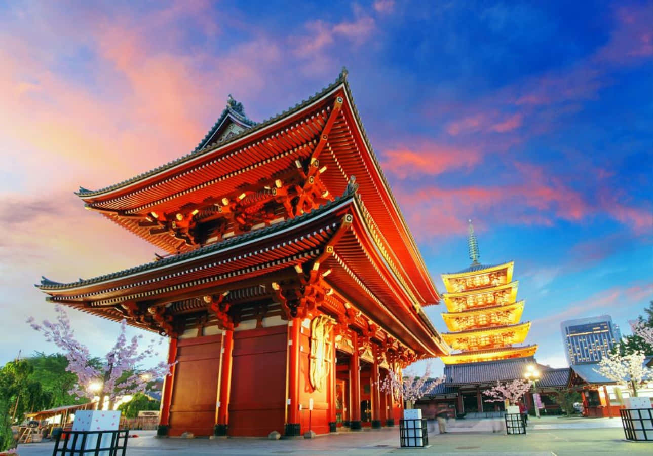 東京 桌布 壁紙 — 一座宏偉的紅色日本寺廟，掛著發光的燈籠，矗立在充滿活力的黃昏天空下，天空中有粉紅色和藍色的雲彩。