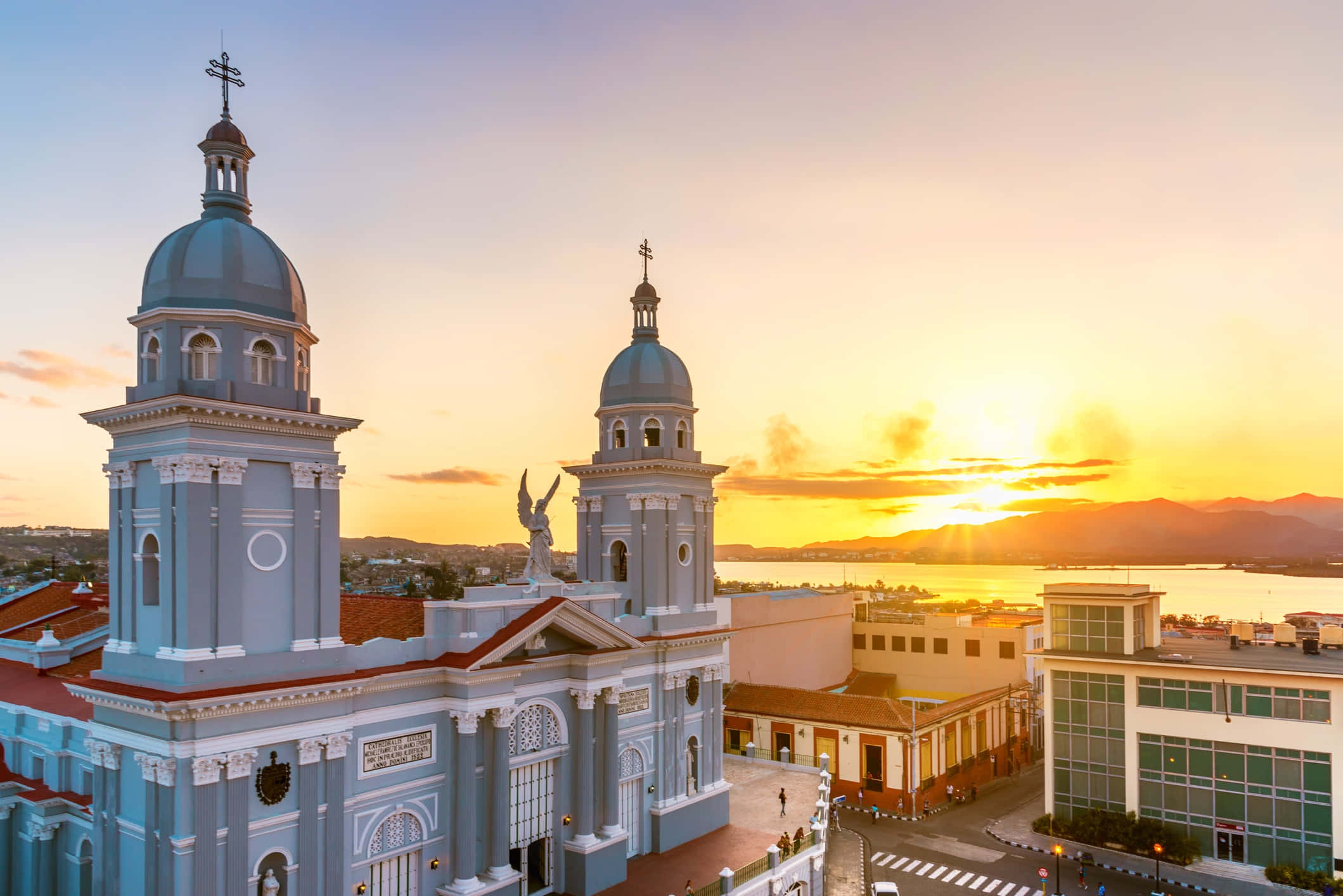 Cuba 桌布 壁紙 — 一座宏偉的藍色大教堂，擁有雙圓頂，在金色夕陽的天空下矗立於沿海城市之上。