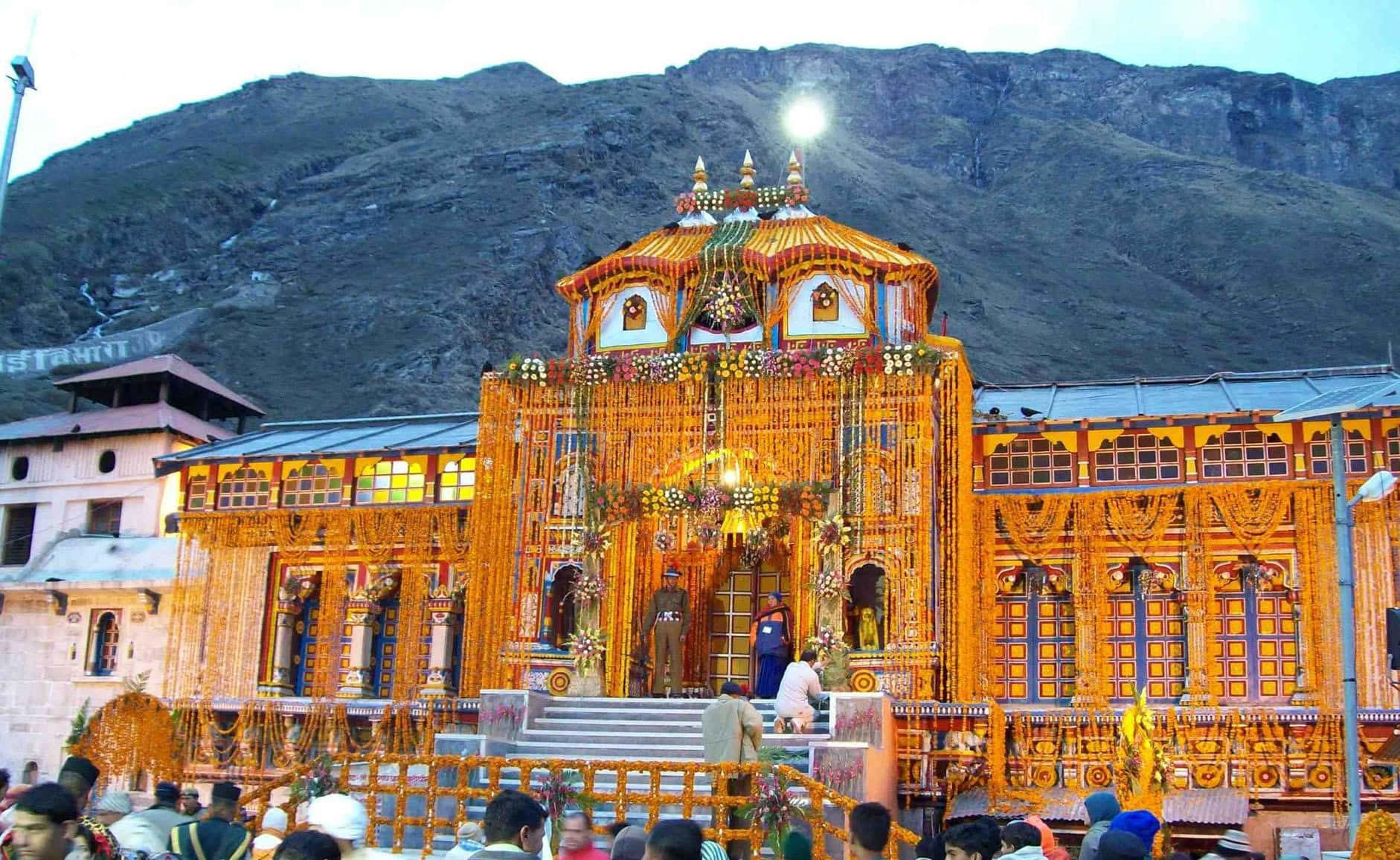 Kedarnath 桌布 壁紙 — 一座宏偉的金色寺廟，飾以精緻的花環，在黃昏時分雄偉地矗立在崎嶇的山脈背景下。