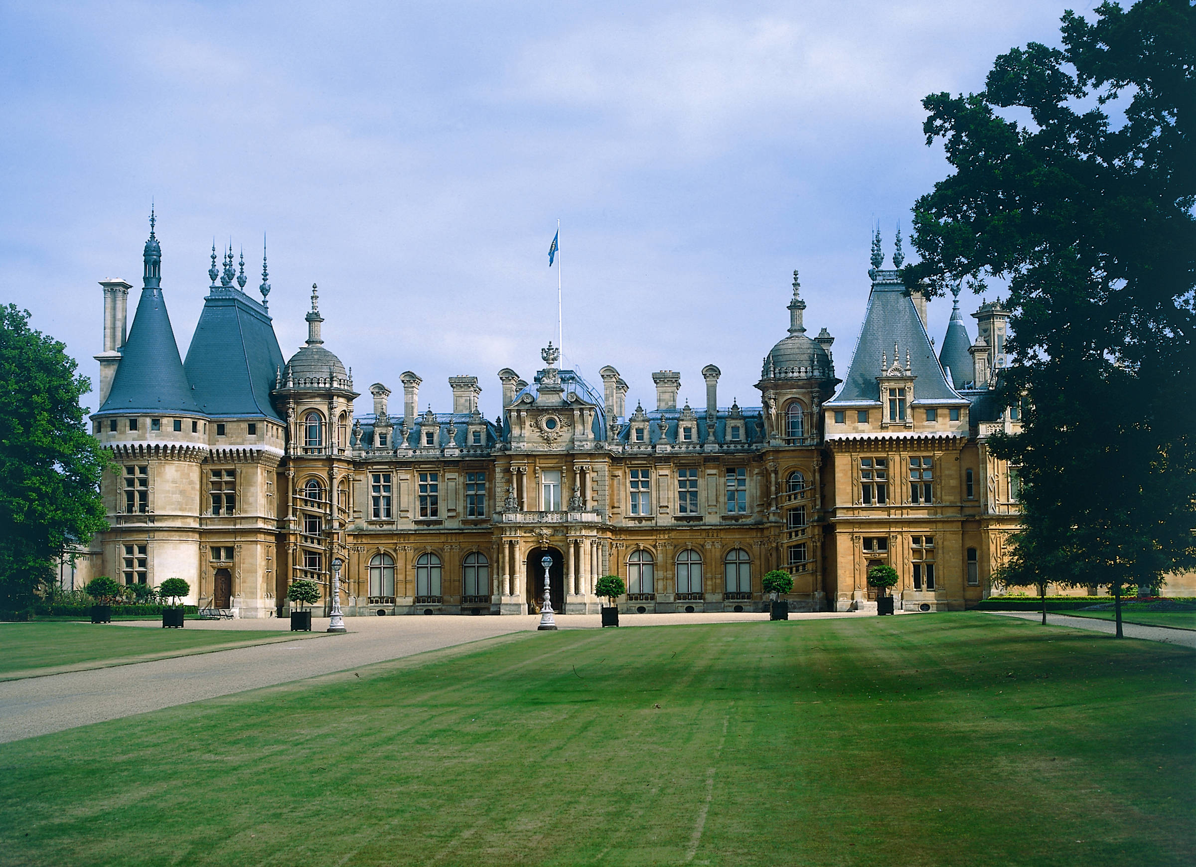 United Kingdom 桌布 壁紙 — 一座宏偉華麗的城堡，擁有藍色圓錐形屋頂和石塔，在柔和的藍天下，雄偉地矗立在鬱鬱蔥蔥的綠色草坪之中。