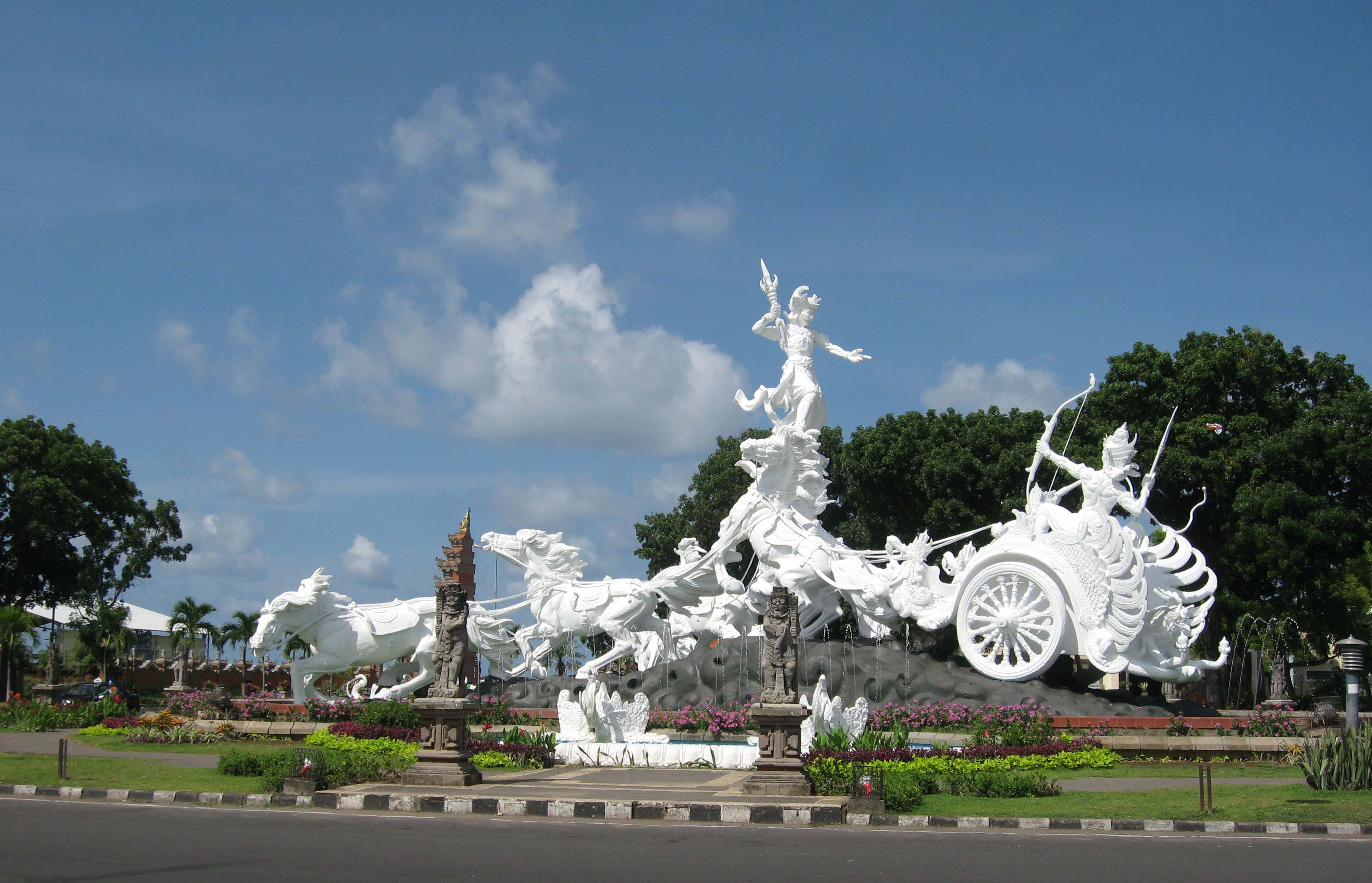 Indonesia 桌布 壁紙 — 一座宏大的白色大理石神話戰車雕塑，由馬匹拉動，背景是晴朗的藍天和蓬鬆的白雲。
