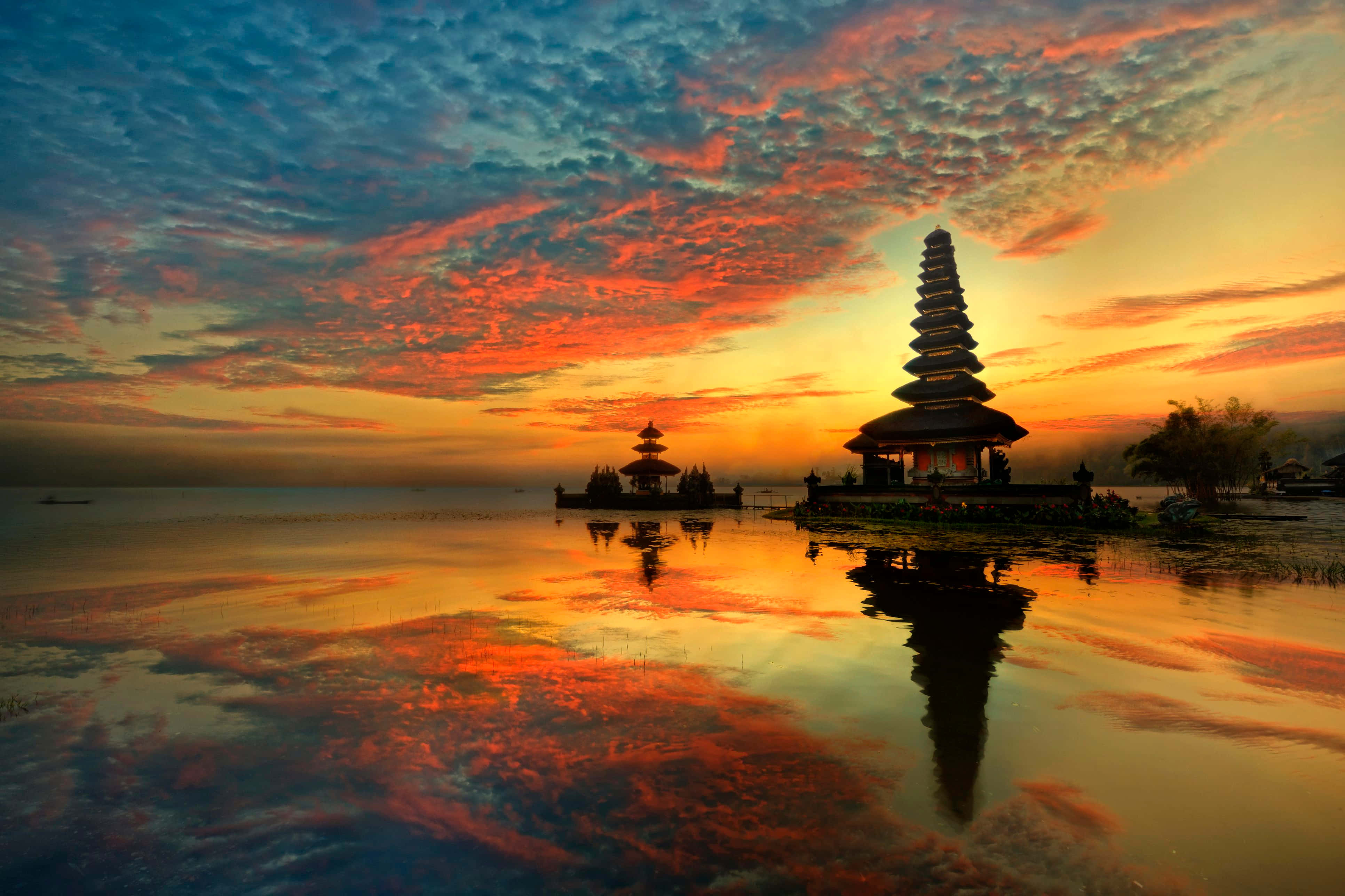 Bali 桌布 壁紙 — 一座寧靜的峇里島寺廟在火紅的日落天空映襯下形成剪影，完美倒映在平靜的水面上。