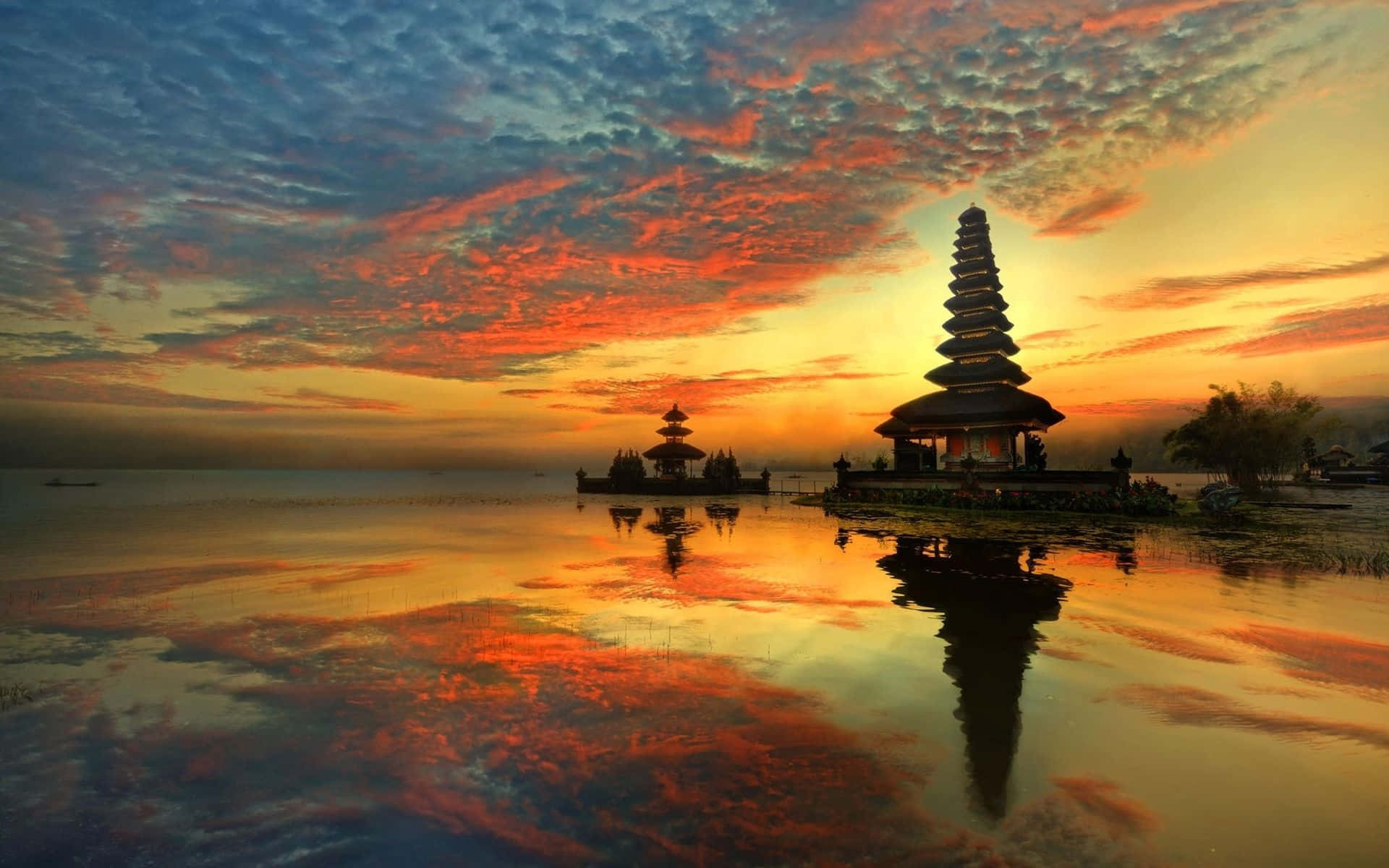 Bali Beach 桌布 壁紙 — 一座寧靜的峇里島寺廟在火紅的日落天空映襯下形成剪影，完美倒映在平靜的水面上。