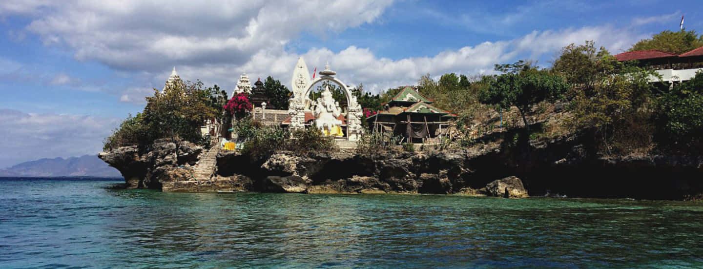 Bali Island 桌布 壁紙 — 一座寧靜的白色寺廟坐落在岩石島上，周圍是碧綠的海水，天空部分多雲。
