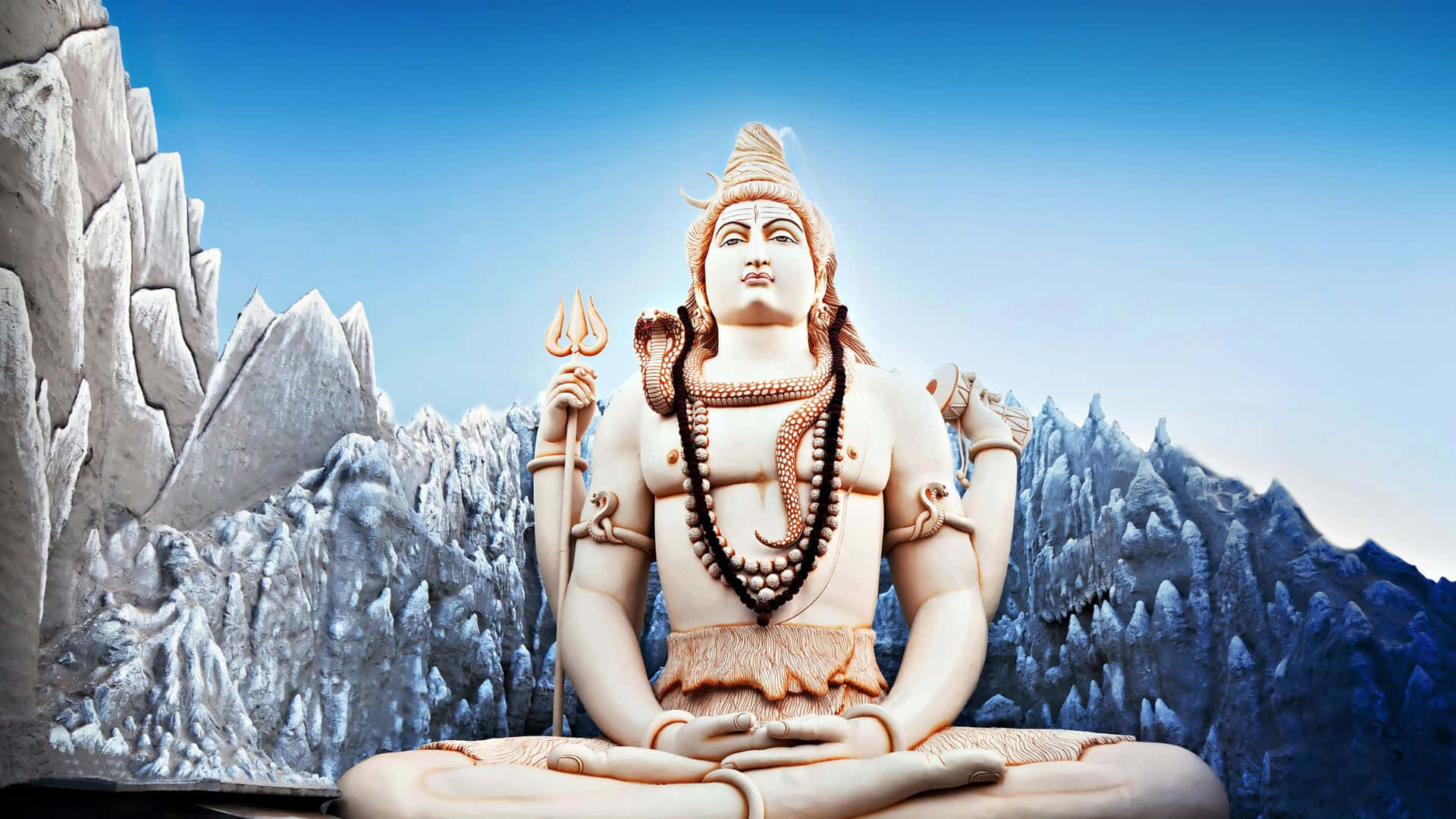 Shiva 桌布 壁紙 — 一座寧靜的白色石雕濕婆神像，在晴朗藍天下盤腿坐在山頂上冥想。