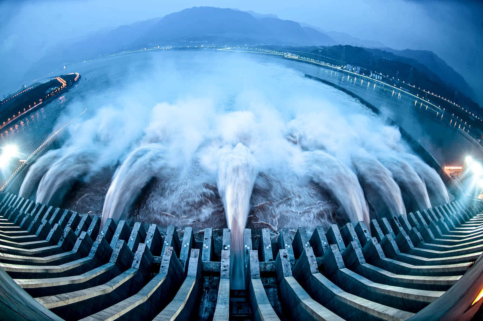 Energy 桌布 壁紙 — 一座巨大的水壩在黃昏時釋放出大量水流，霧氣升騰，燈光照亮彎曲的混凝土結構。