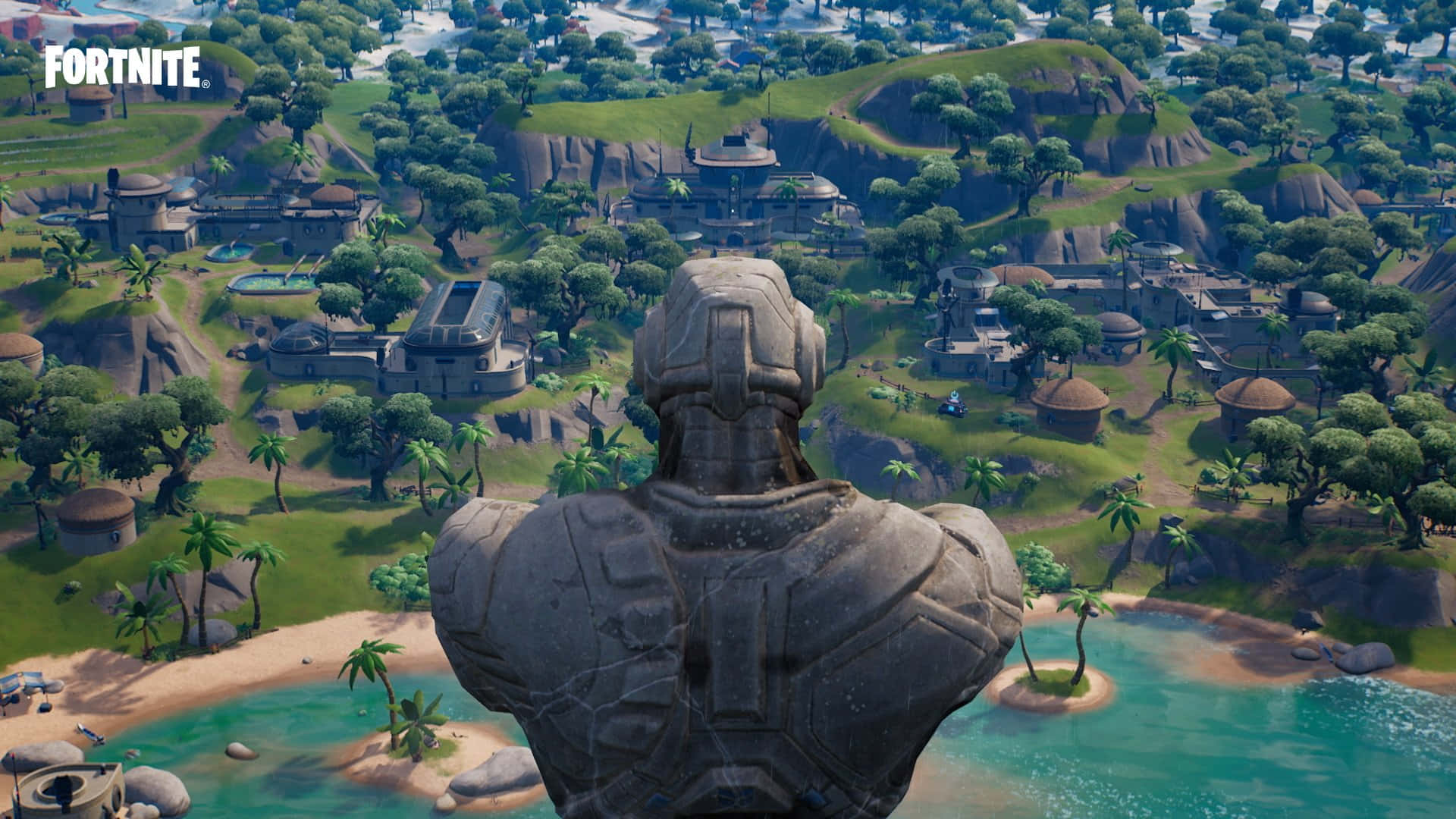 Fortnite Chapter 3 桌布 壁紙 — 一座巨大的石像俯瞰著一個熱帶Fortnite島嶼村莊，村莊裡有棕櫚樹和碧綠的海水。