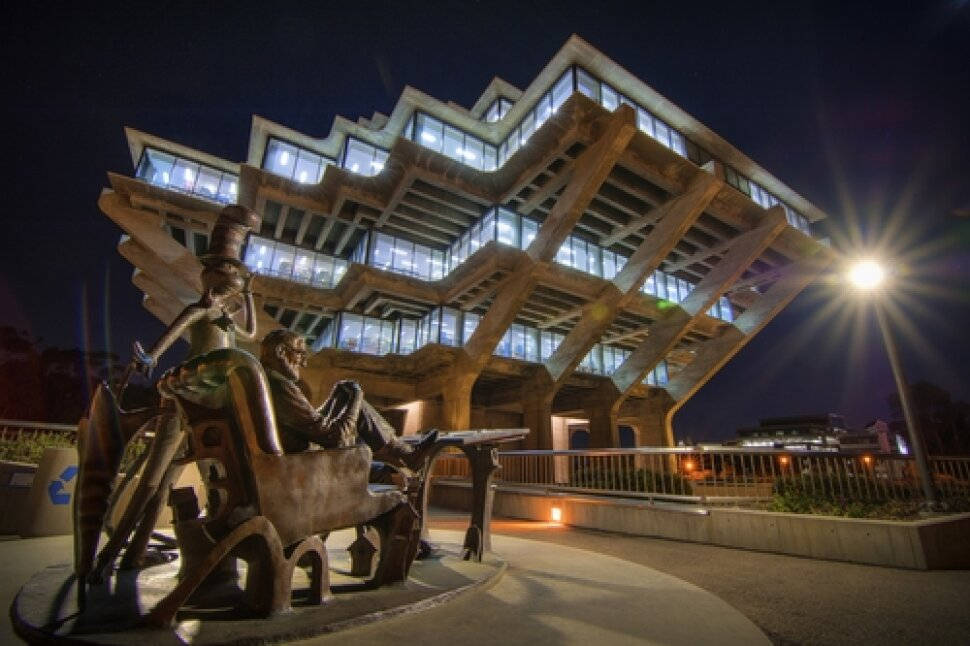 Dr. Seuss UCSD 壁紙 — 一座引人注目的現代建築，帶有發光的窗戶，矗立在夜晚，被一個明亮的街燈照亮，旁邊是一座兩個人物青銅雕塑。
