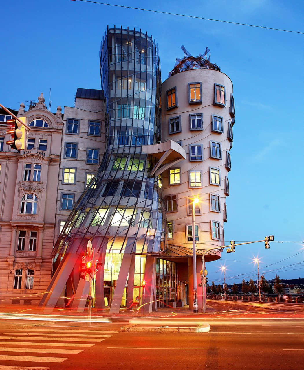 Beautiful Architecture 桌布 壁紙 — 一座引人注目的現代玻璃和鋼鐵建築在暮色天空下戲劇性地扭曲，下方有發光的窗戶和條紋狀的路燈。