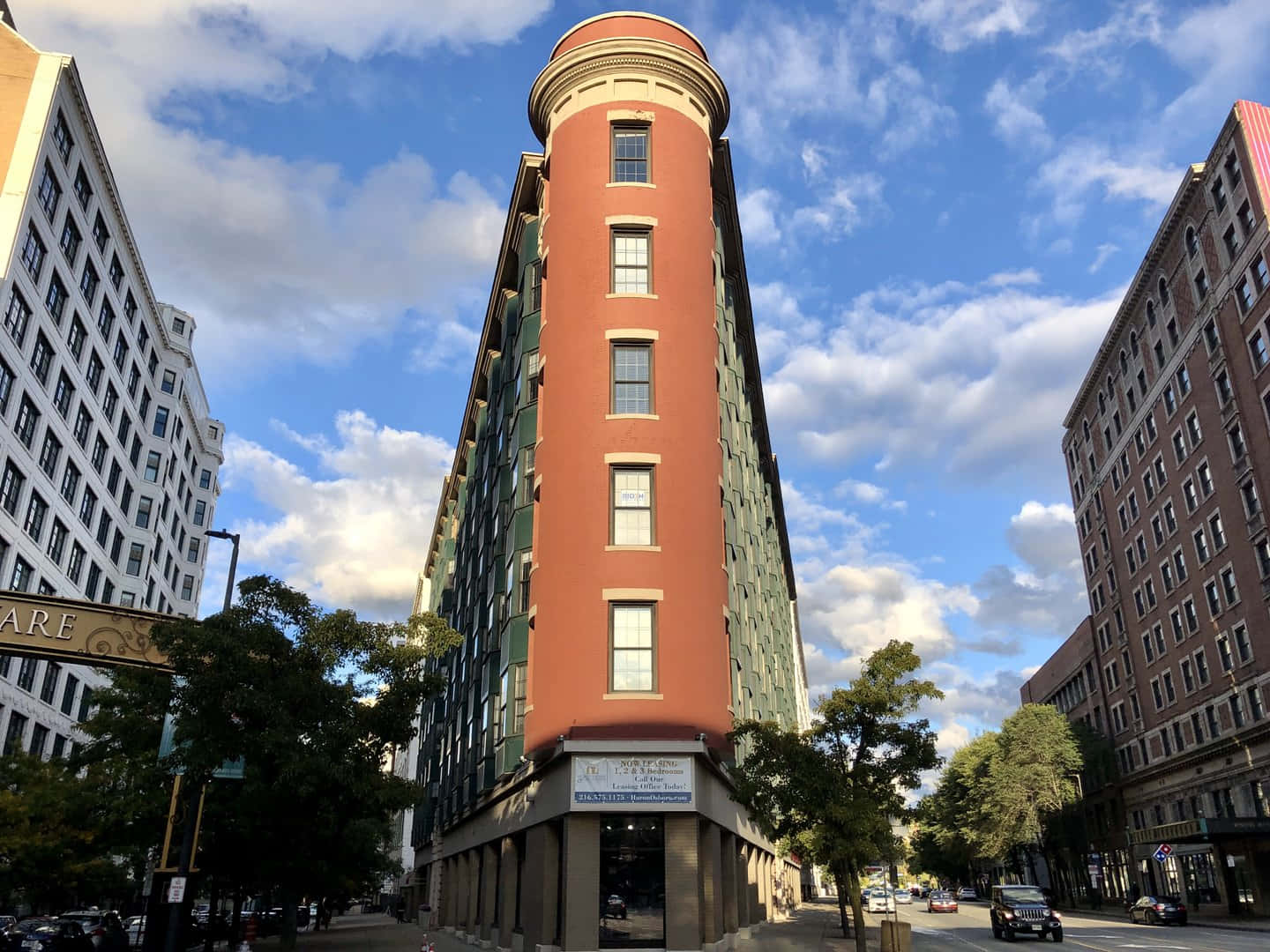 Beautiful Architecture 桌布 壁紙 — 一座引人注目的紅色圓柱形建築聳立在城市街道上，上方是晴朗的藍天和蓬鬆的白雲。