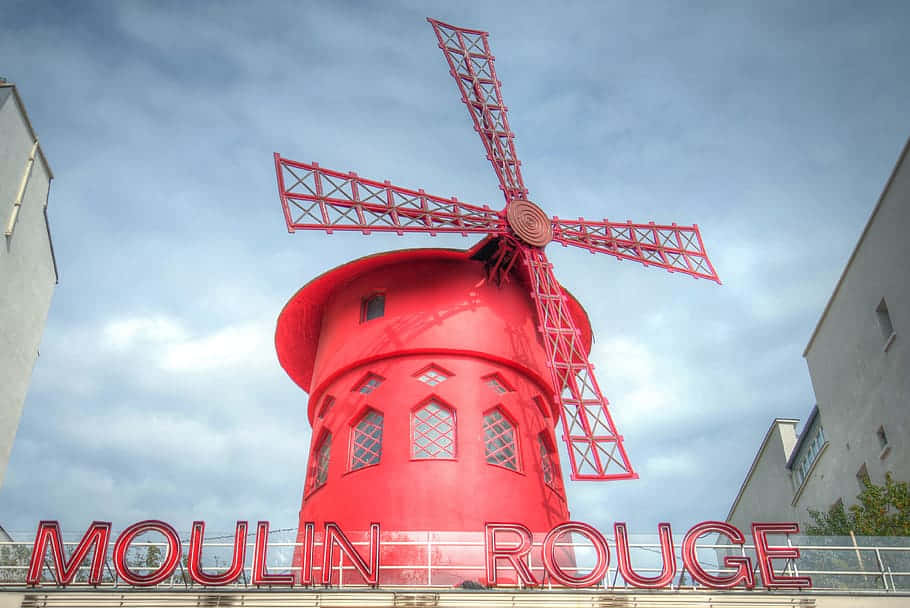  壁紙 — 一座引人注目的紅色風車，帶有'MOULIN ROUGE'標誌，在建築物框住的陰天背景下高高聳立。