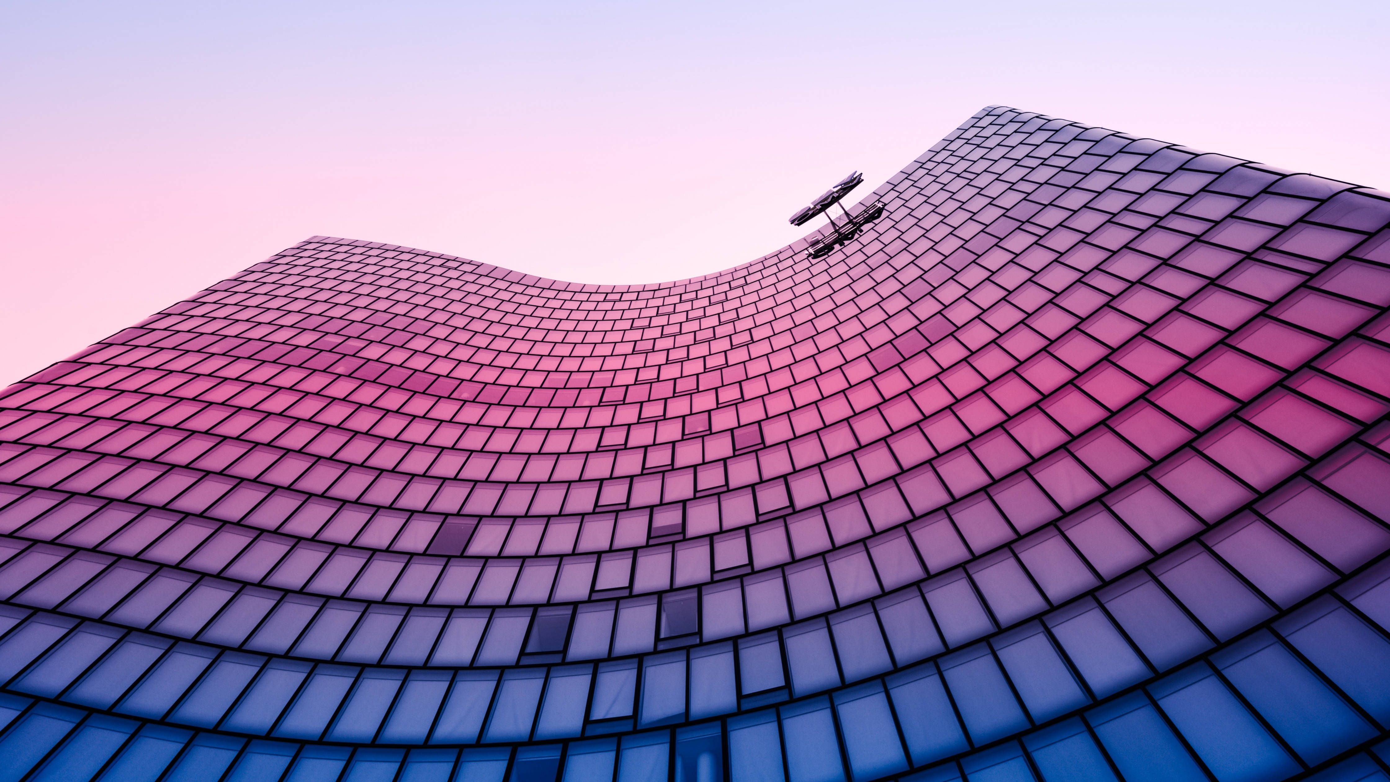 Architecture 桌布 壁紙 — 一座未來主義的波浪形玻璃建築在柔和的粉紅色和紫色暮色天空中向上彎曲。