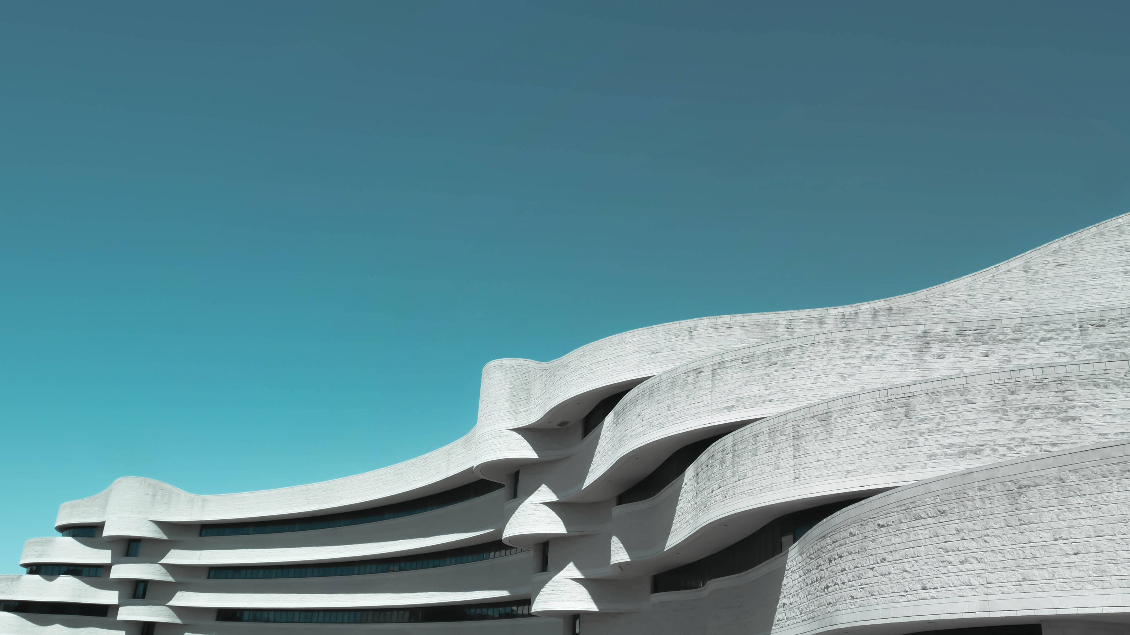 Museum 桌布 壁紙 — 一座未來主義的白色建築，帶有流暢的曲線和紋理表面，矗立在清澈的藍天下。